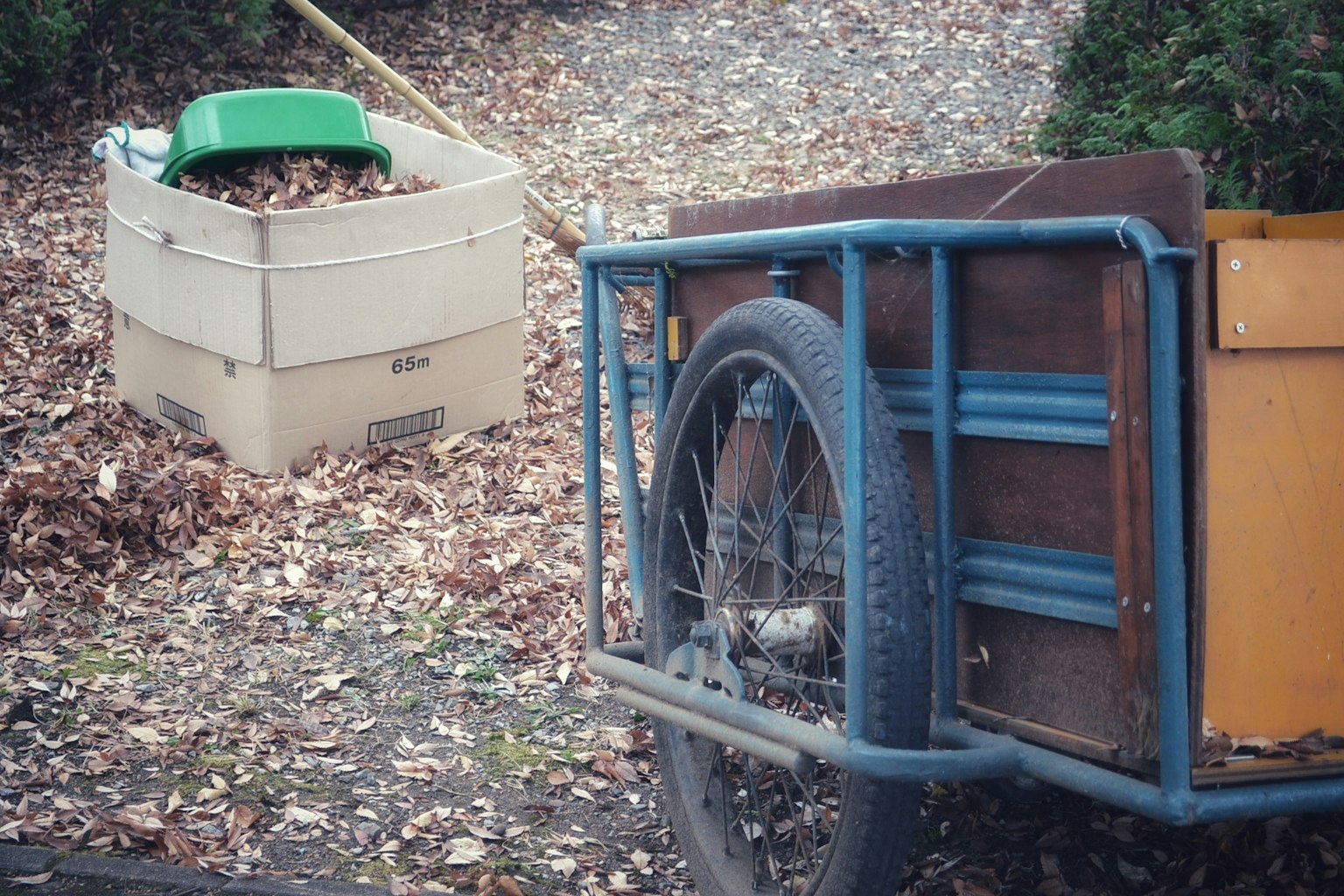 Remolque de bicicleta con hojas y un contenedor verde en un jardín