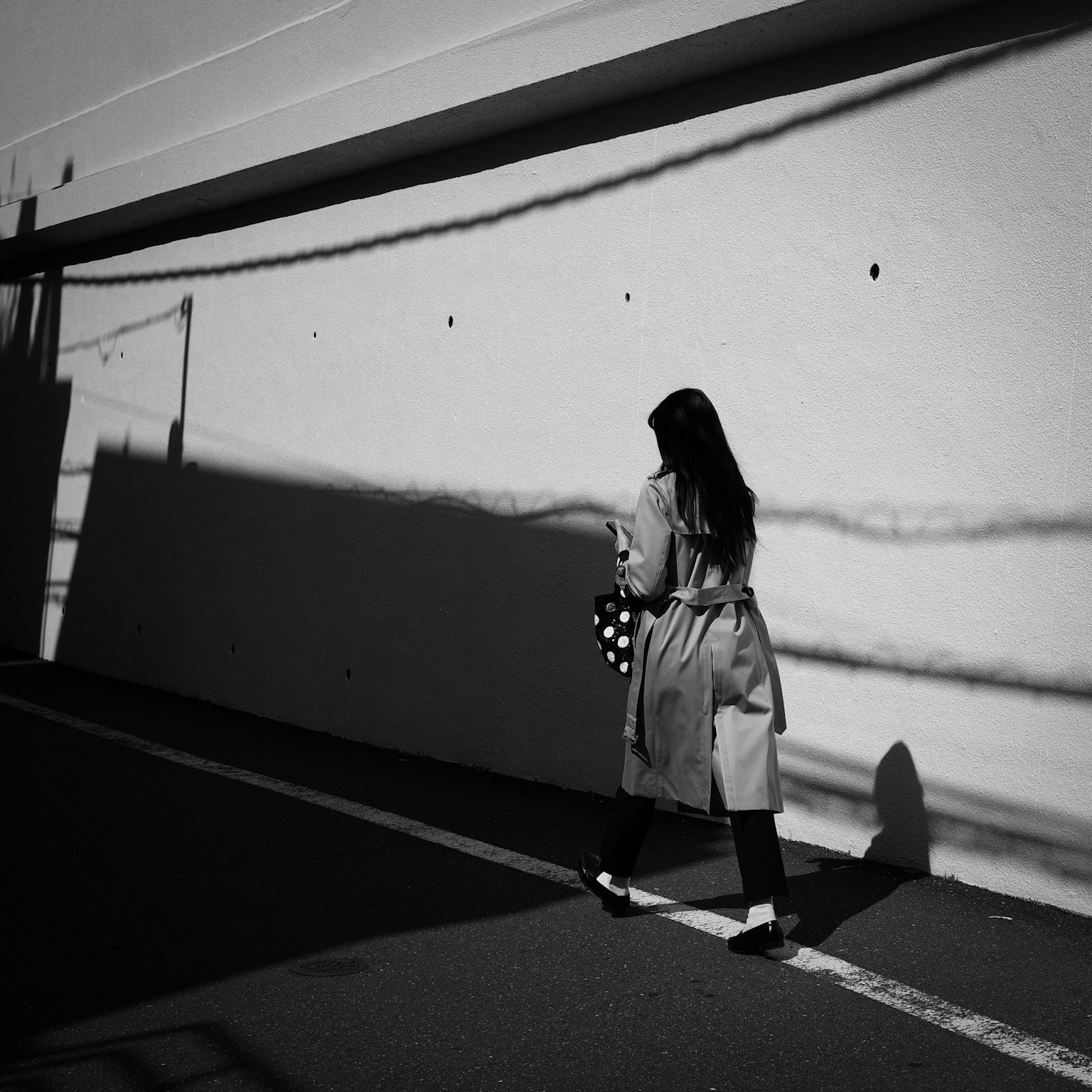 Una donna in trench che cammina con ombre proiettate su un muro in bianco e nero