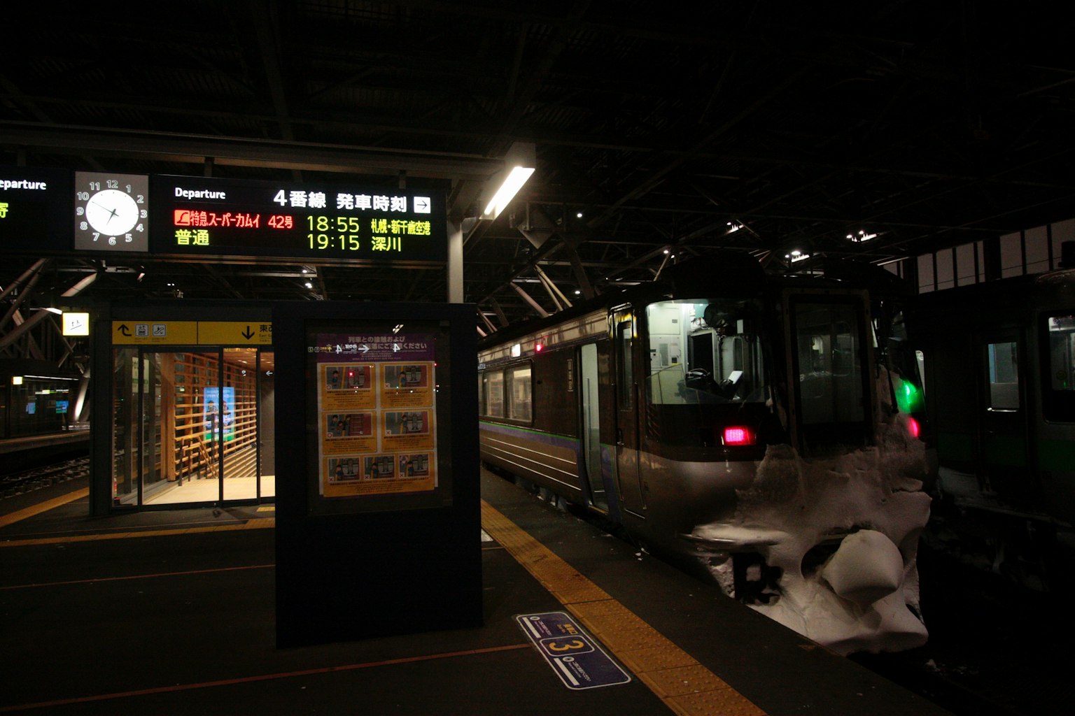 Train stopped at a dimly lit station with digital display of station names