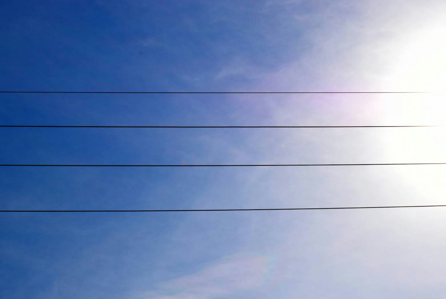Kabel listrik di bawah langit biru cerah dan sinar matahari