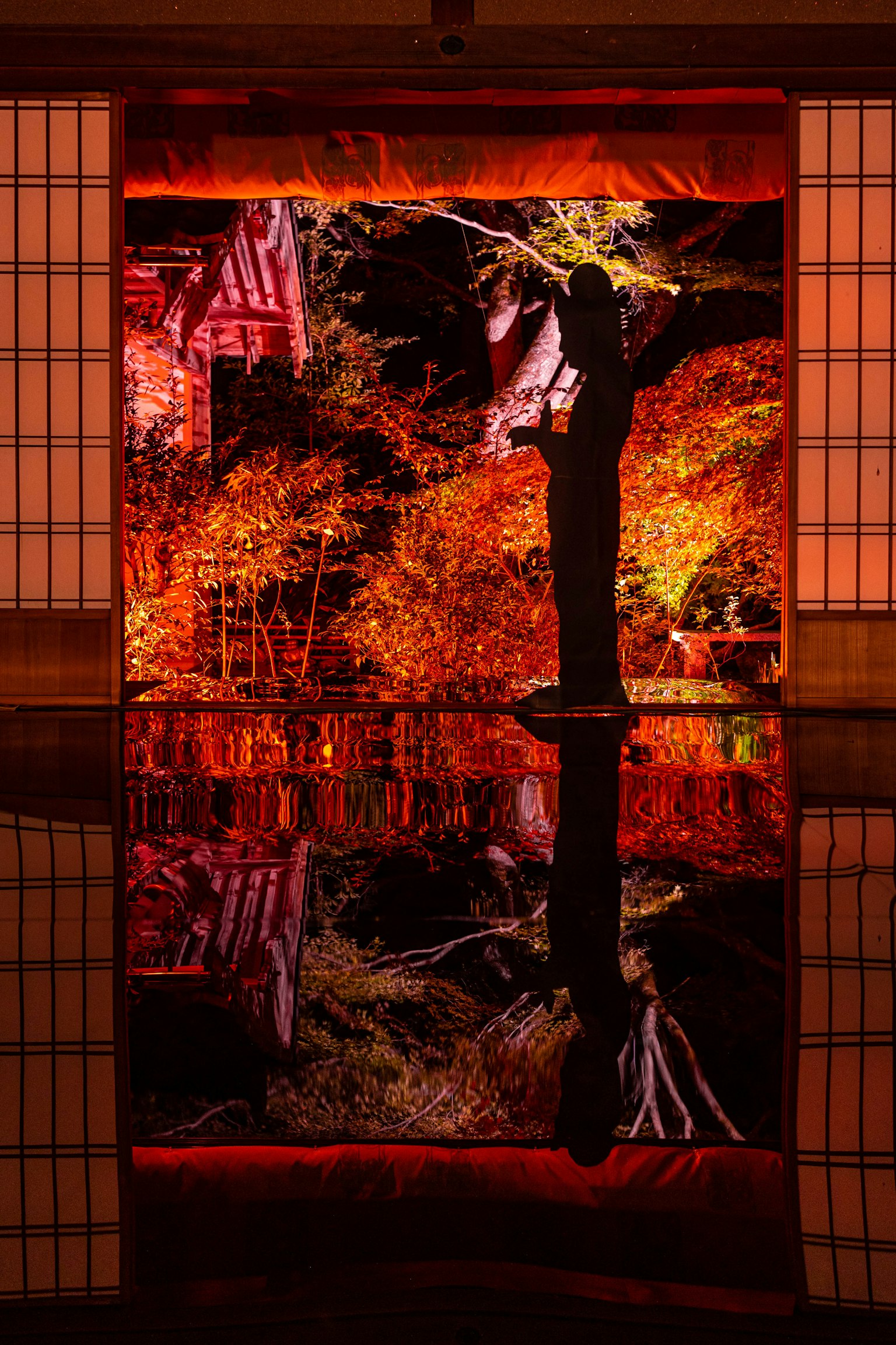 Silhouette of a woman standing on a reflective surface with autumn leaves and traditional Japanese background