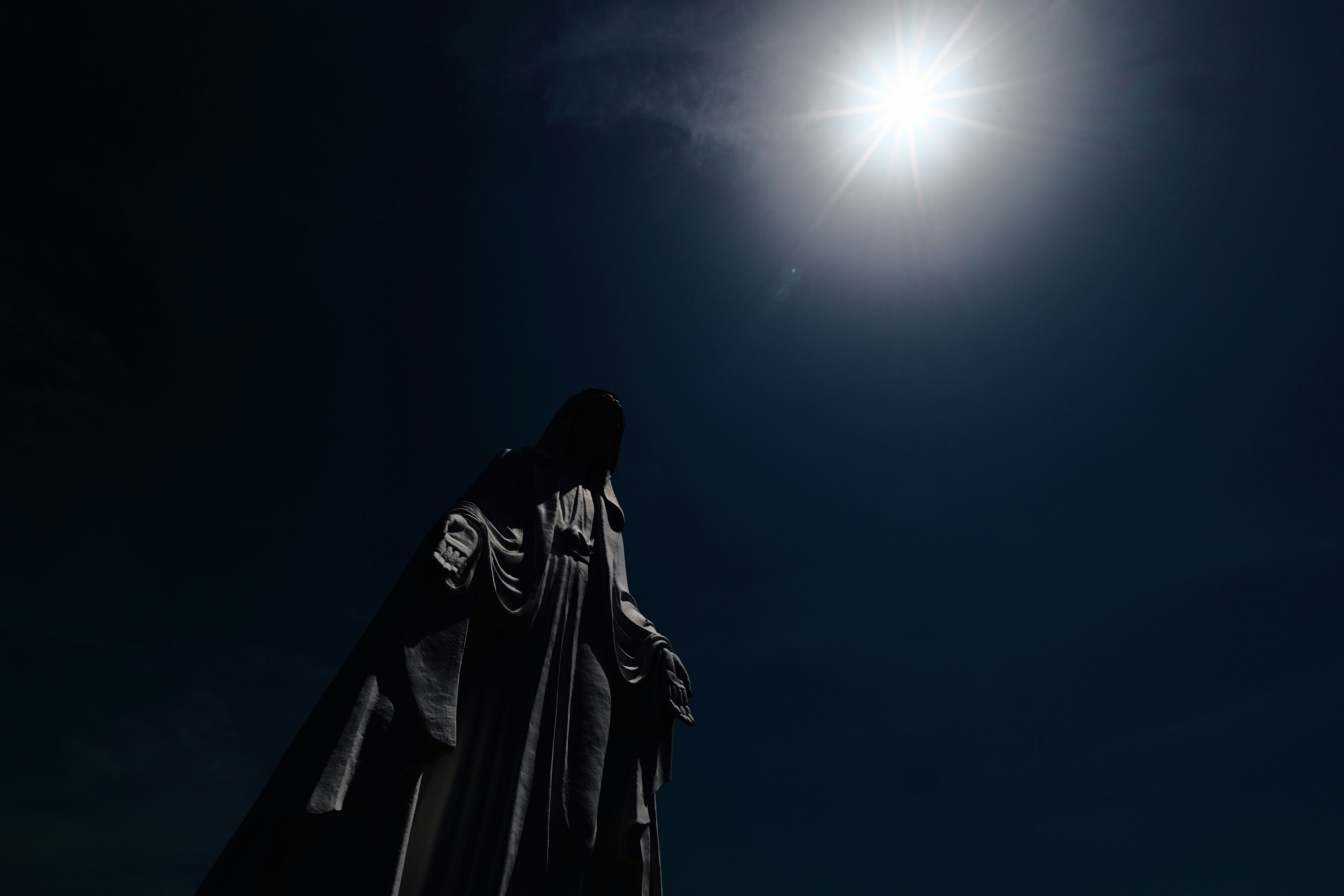 Silhouette d’une statue de la Vierge Marie sous un ciel sombre