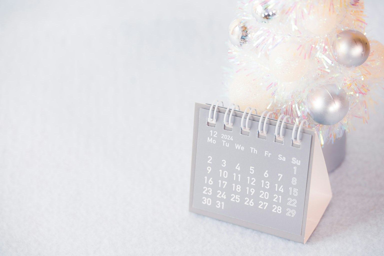 Sebuah kalender di samping pohon Natal putih dengan ornamen perak