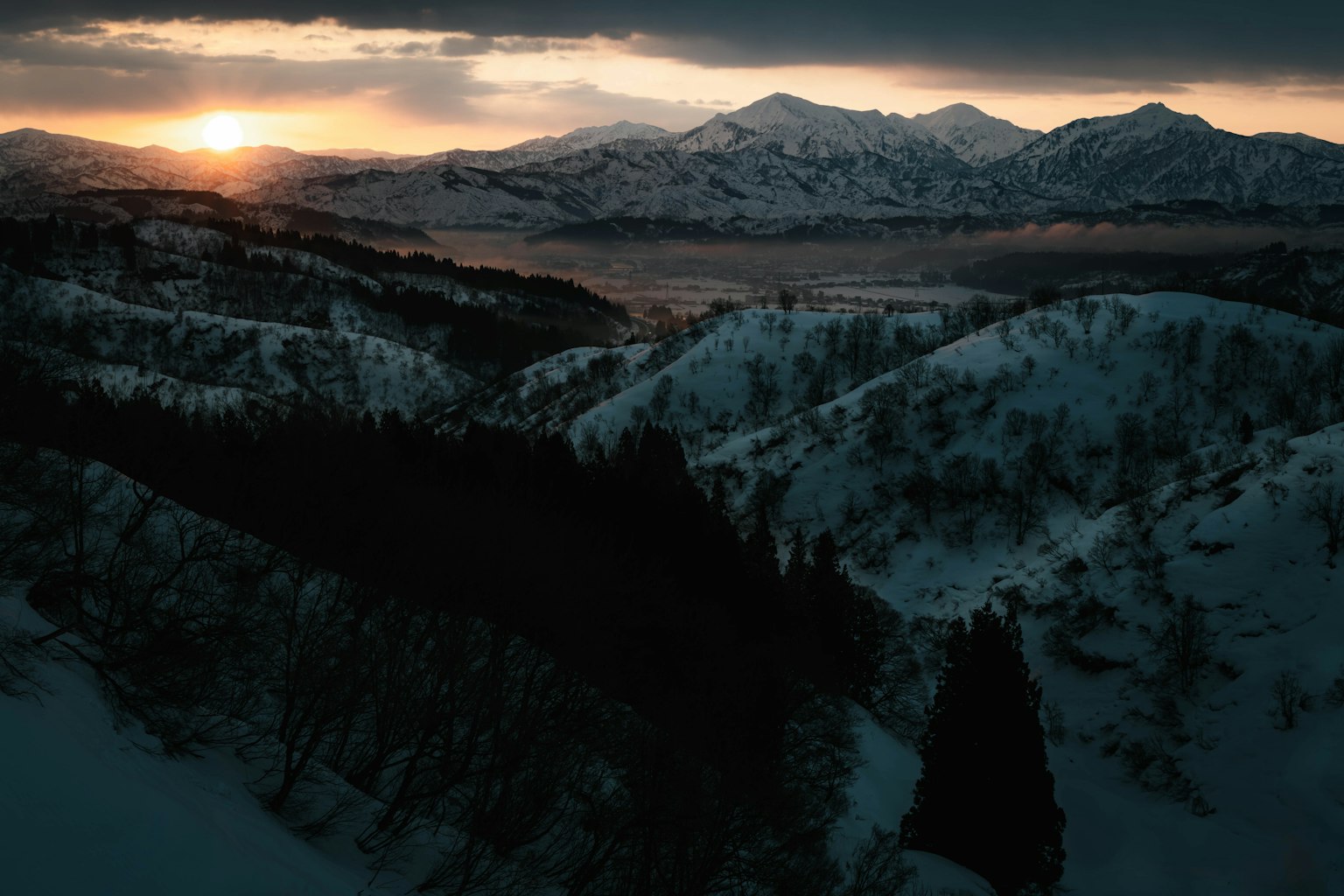 Snow-covered mountains with valleys and a sunset in the background