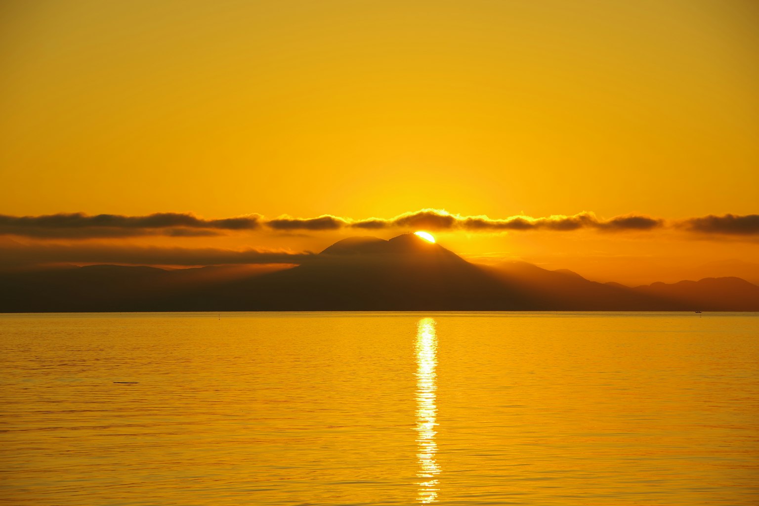 Wunderschöner Sonnenuntergang über einem Berg mit orangefarbenem Himmel und reflektierender Wasseroberfläche