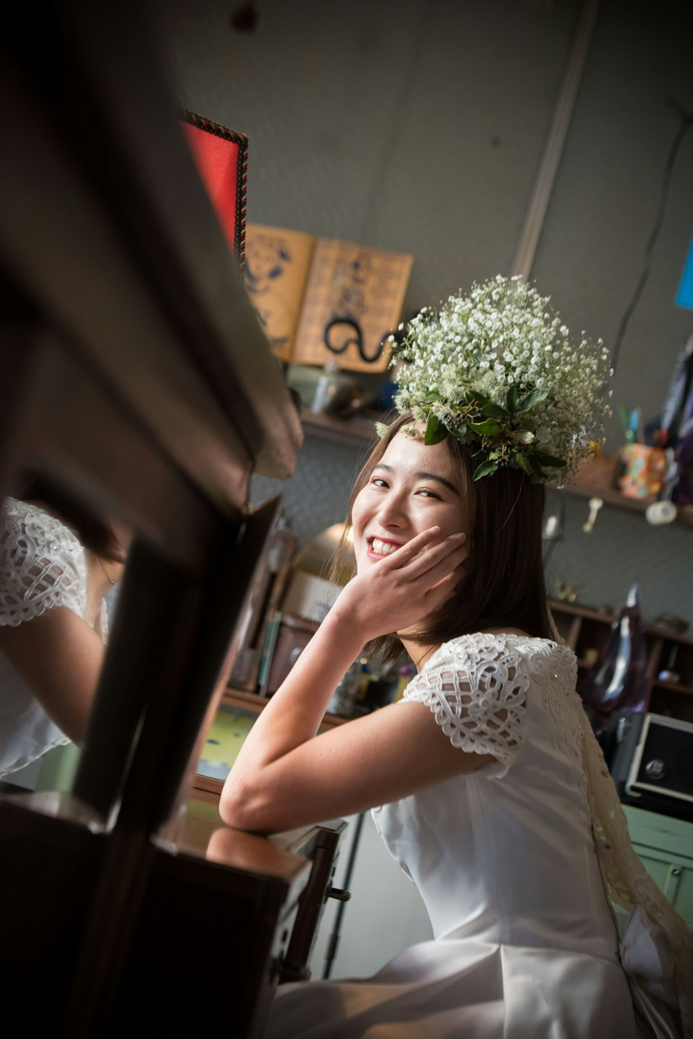 Indoor portrait scene of a smiling woman wearing a flower crown touching her cheek