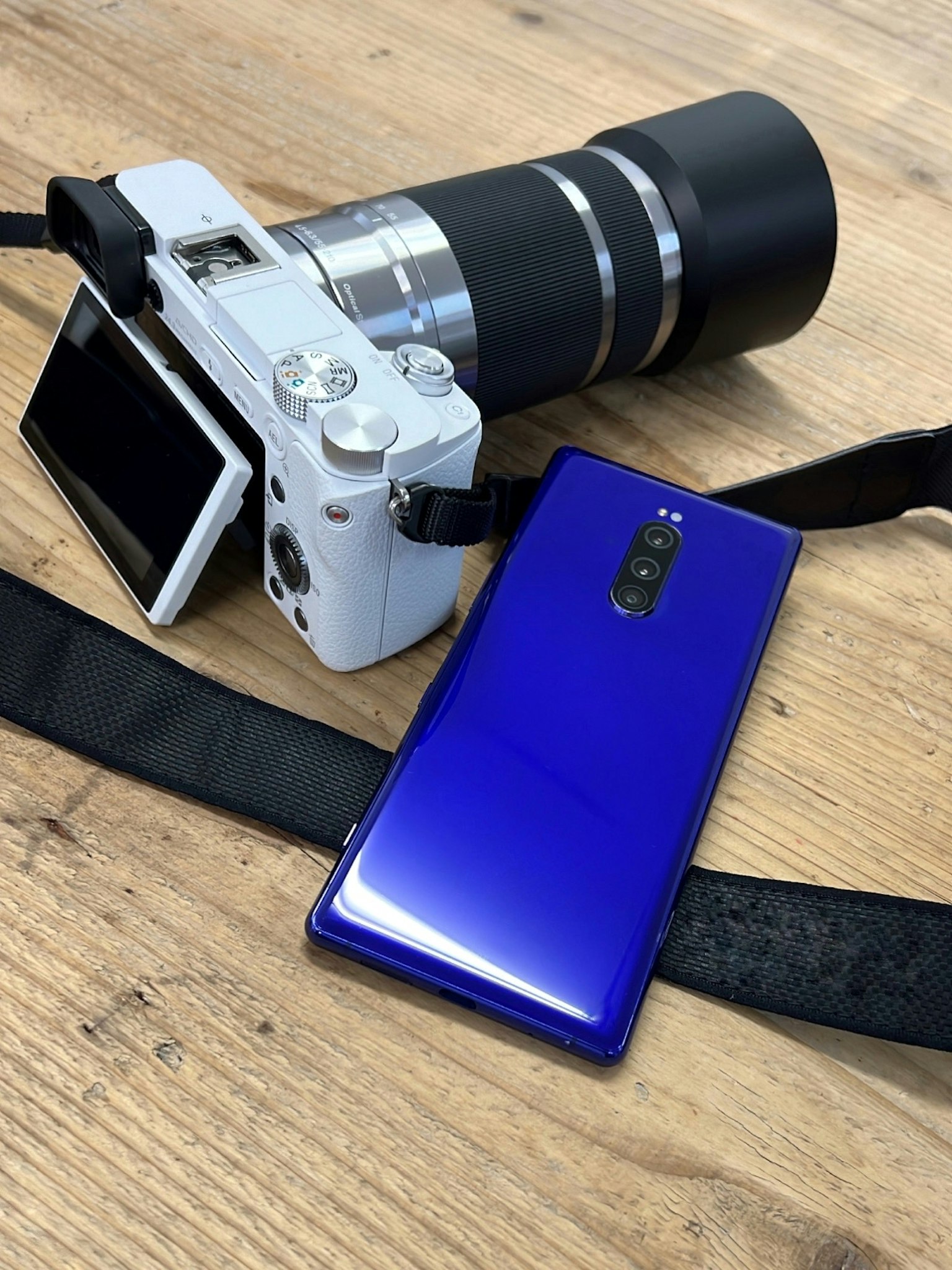 Eine weiße Kamera und ein blauer Smartphone auf einem Holztisch platziert