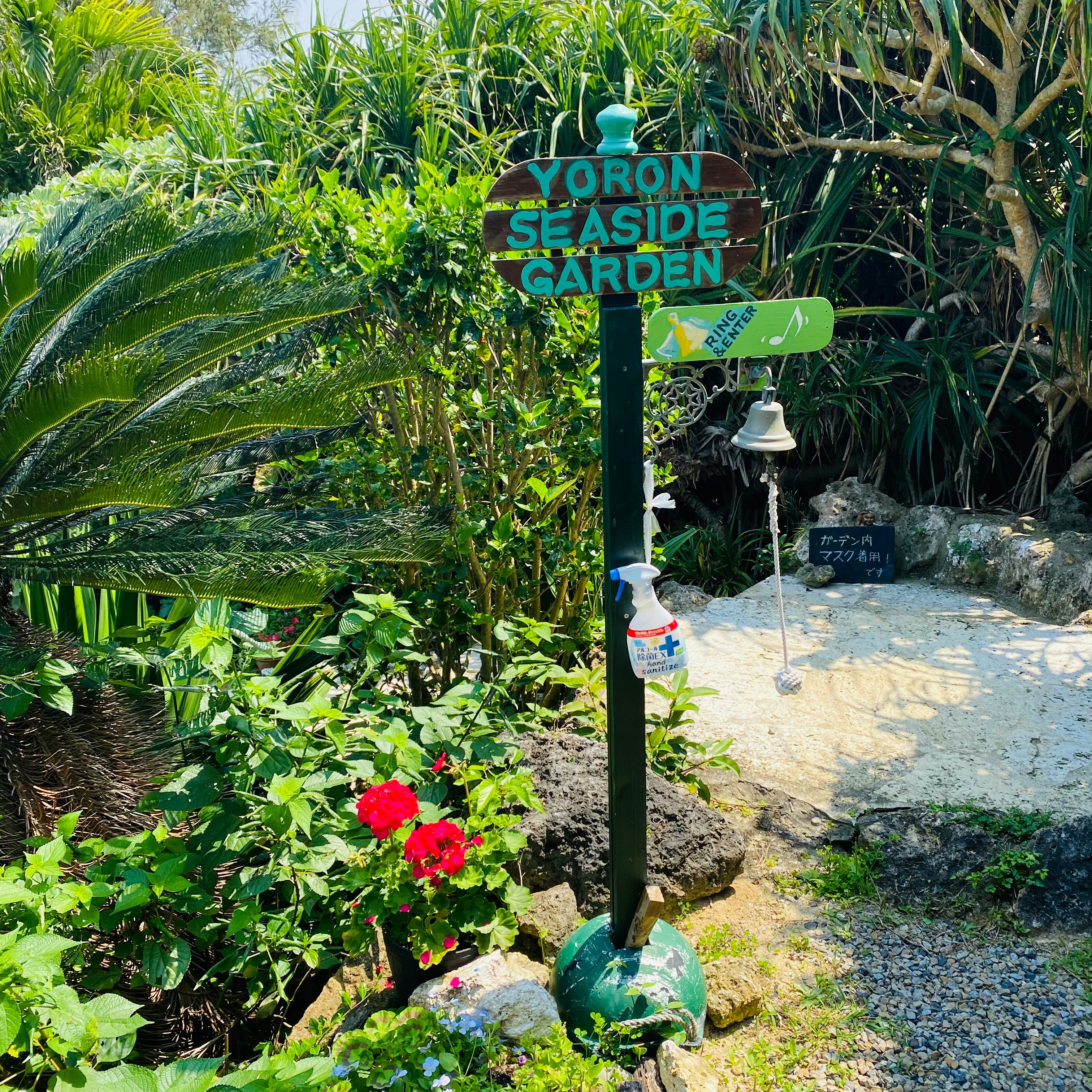 熱帯の庭園の小道にある「YORON SEASIDE GARDEN」の看板と花