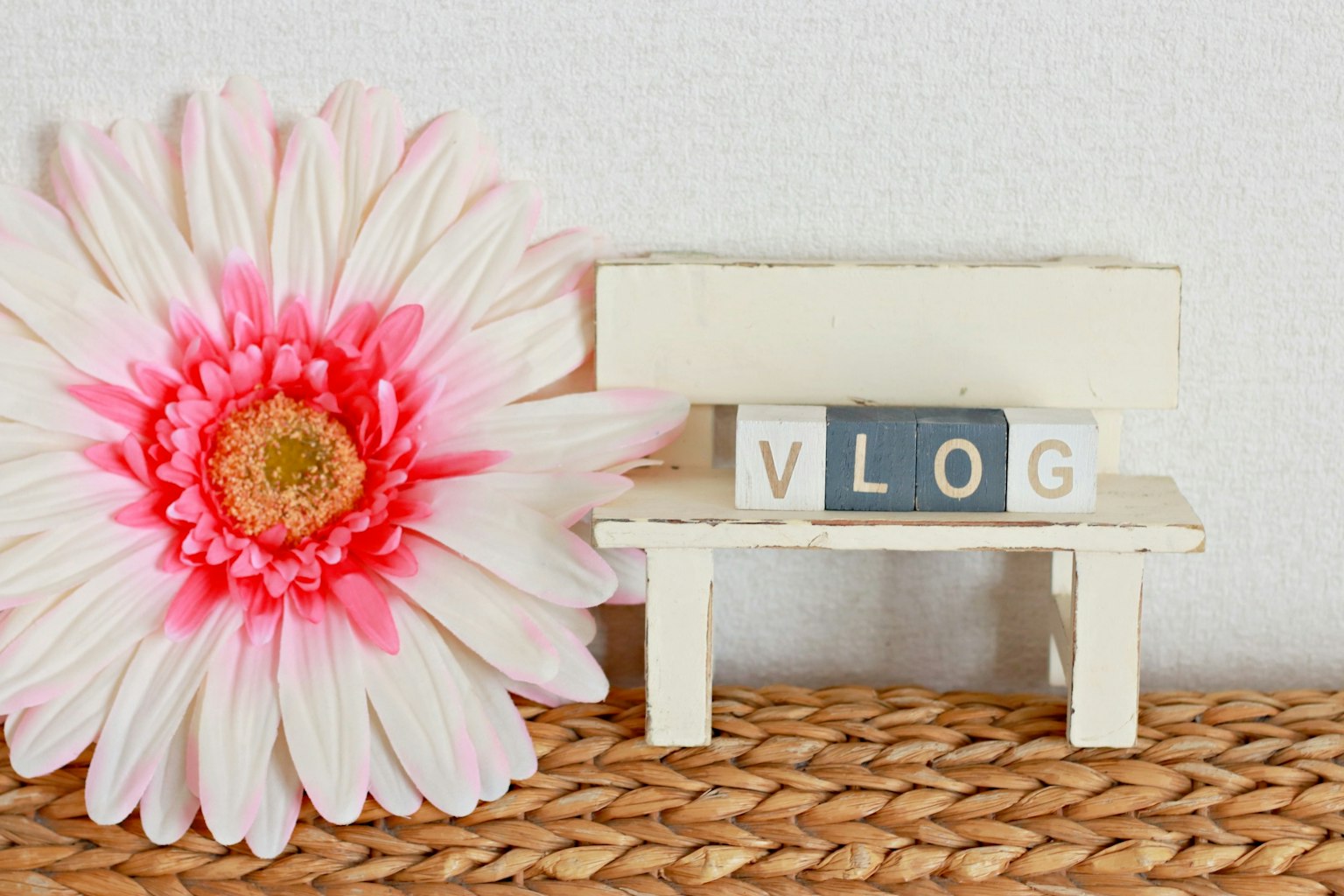 Un pequeño banco blanco con la palabra 'VLOG' en letras de bloque junto a una flor rosa