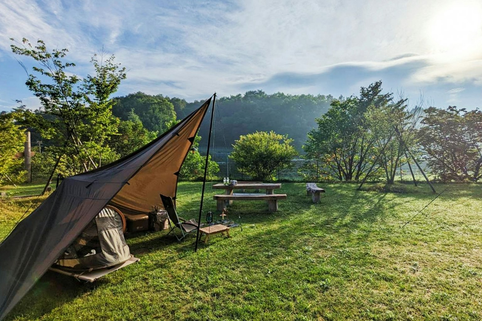Scena di campeggio con una tenda e un tavolo di legno su un prato verde