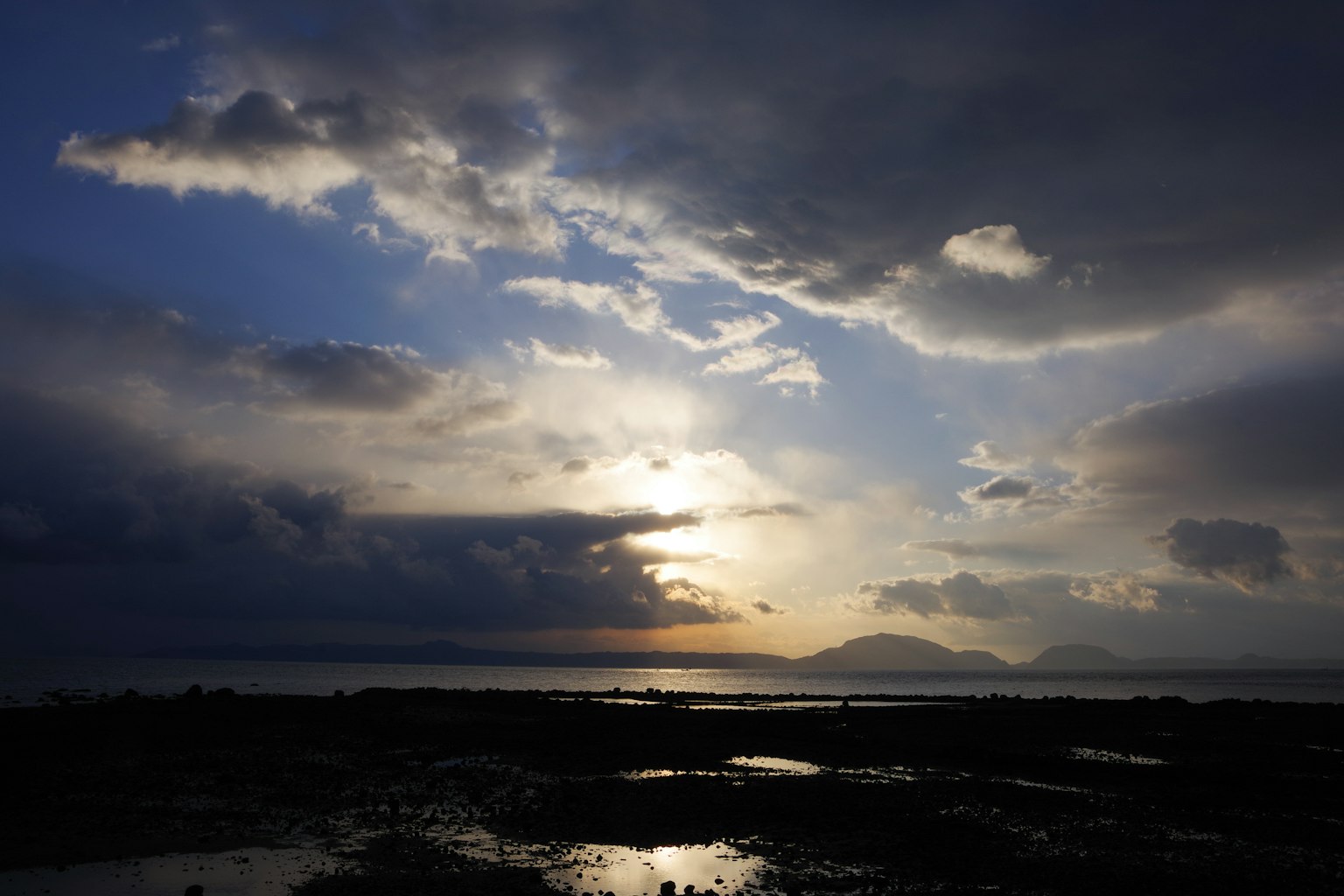 Cielo dramático con luz rompiendo a través de nubes oscuras silueteando montañas y agua