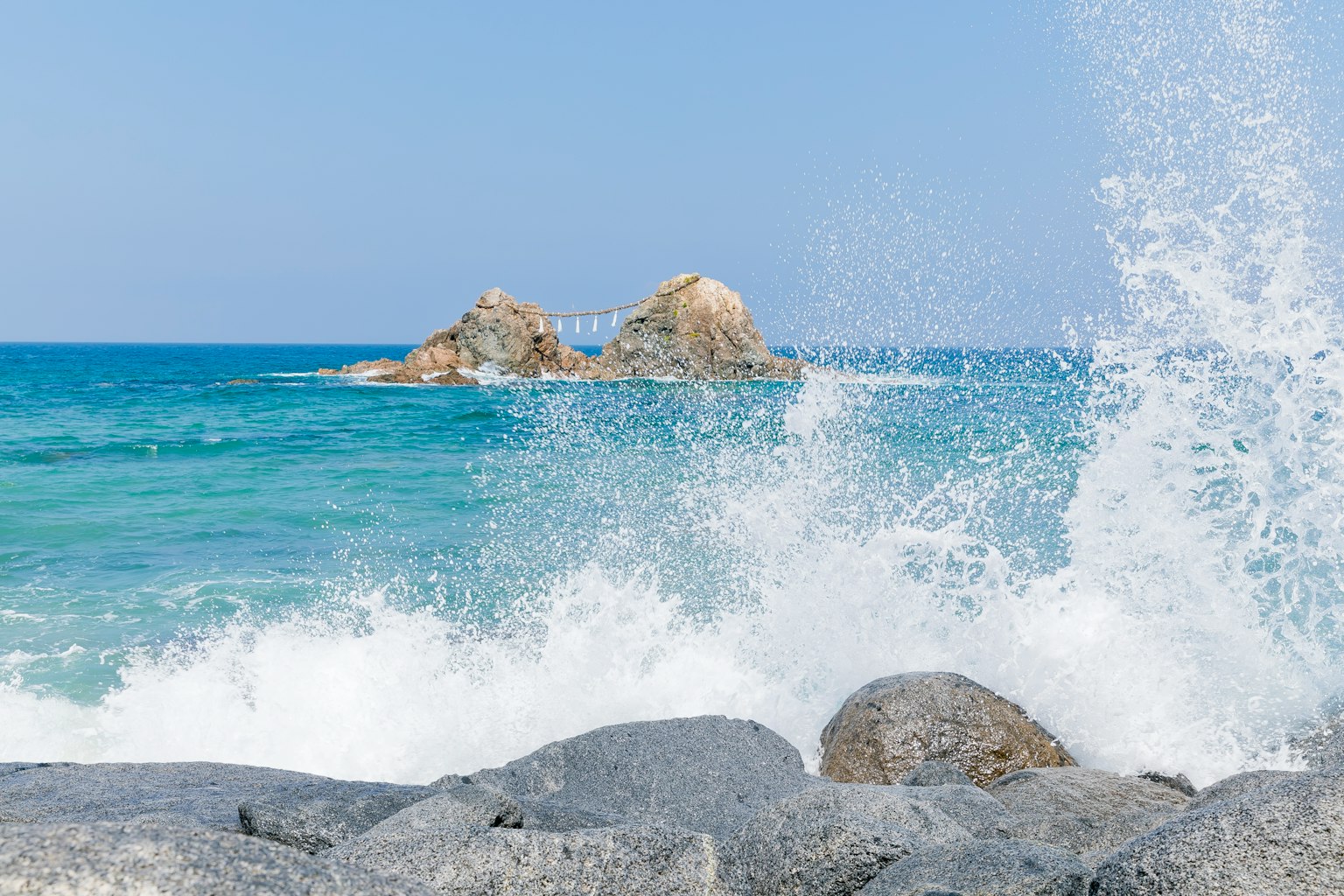 Vagues s'écrasant sur des rochers avec une île au loin dans une mer bleue