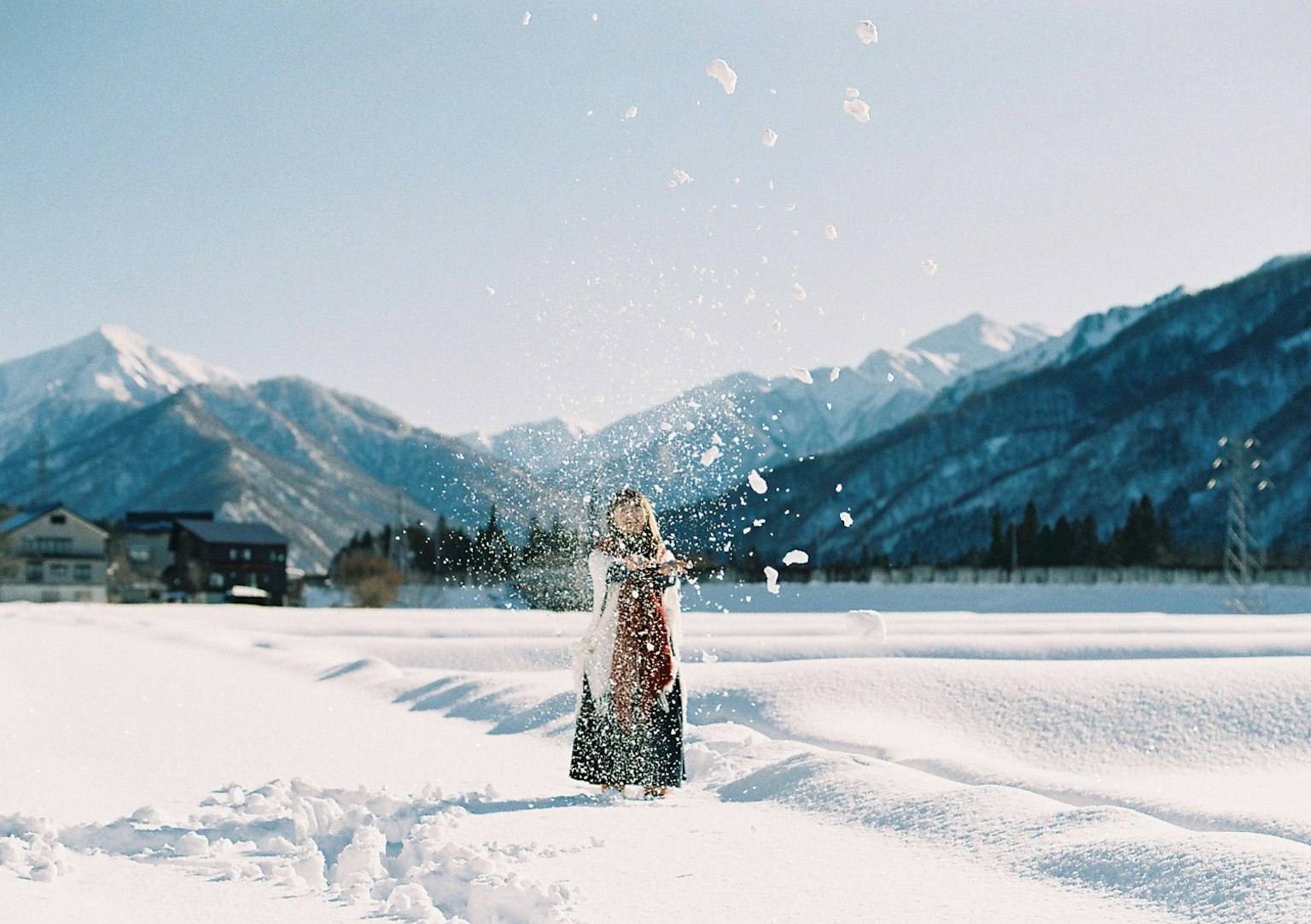 Mujer lanzando nieve en un paisaje nevado con hermosas montañas al fondo