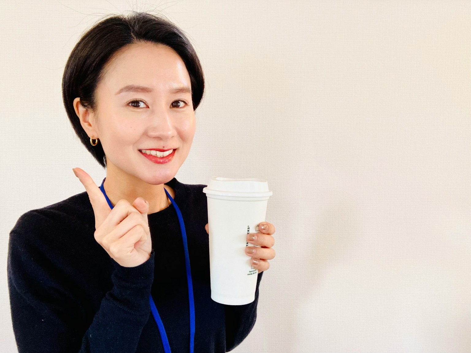 Mujer sonriendo mientras sostiene una taza blanca y señala con el dedo