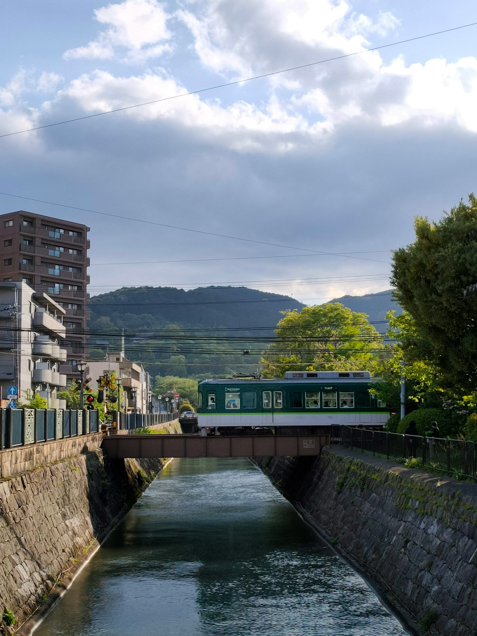 Treno verde che attraversa un fiume con montagne e edifici nei dintorni