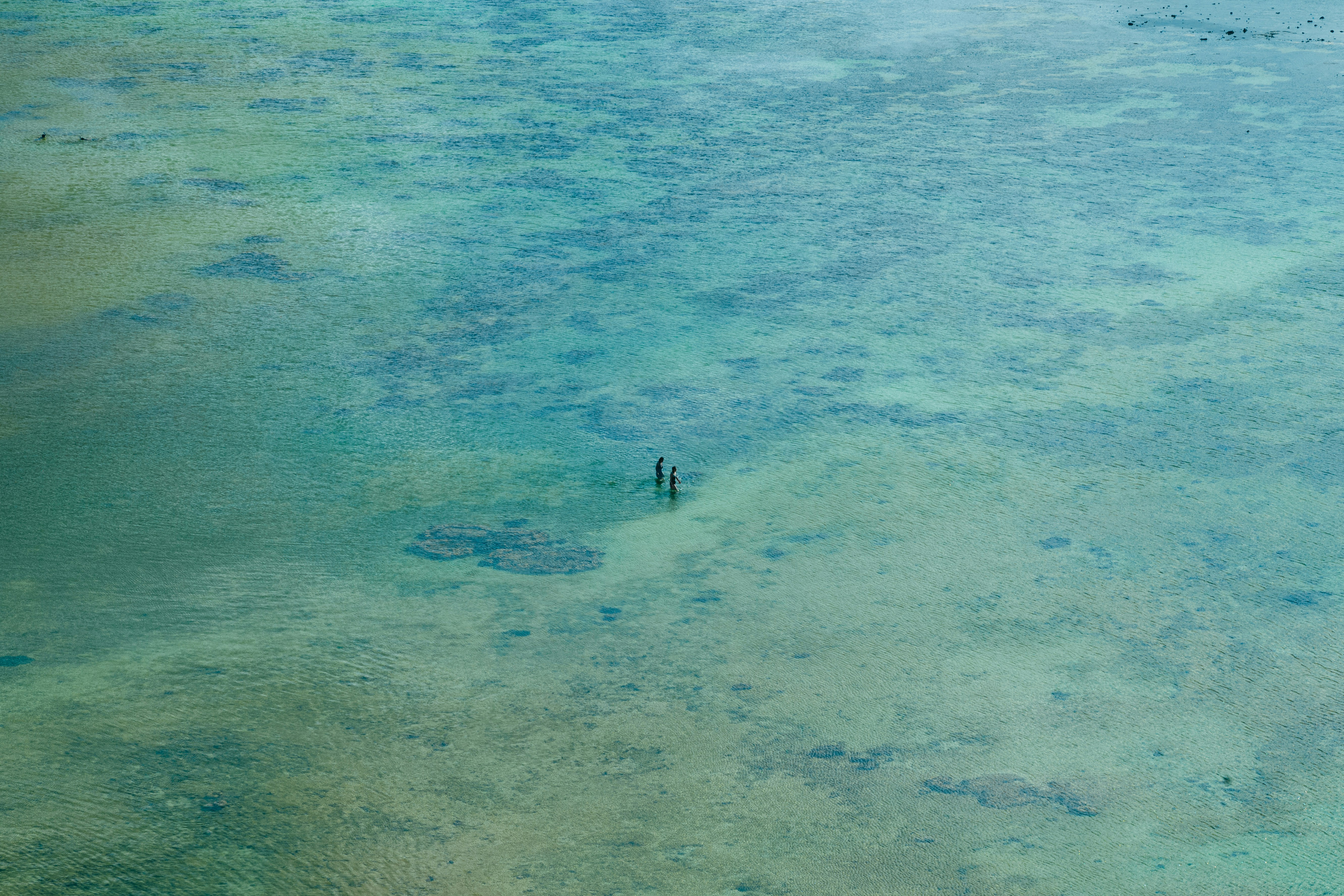 広い浅瀬の海で泳ぐ人影のある風景