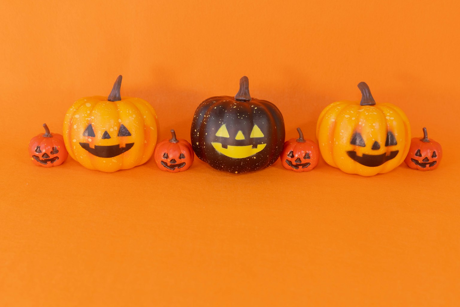 Zucche di Halloween allineate su uno sfondo arancione con volti sorridenti