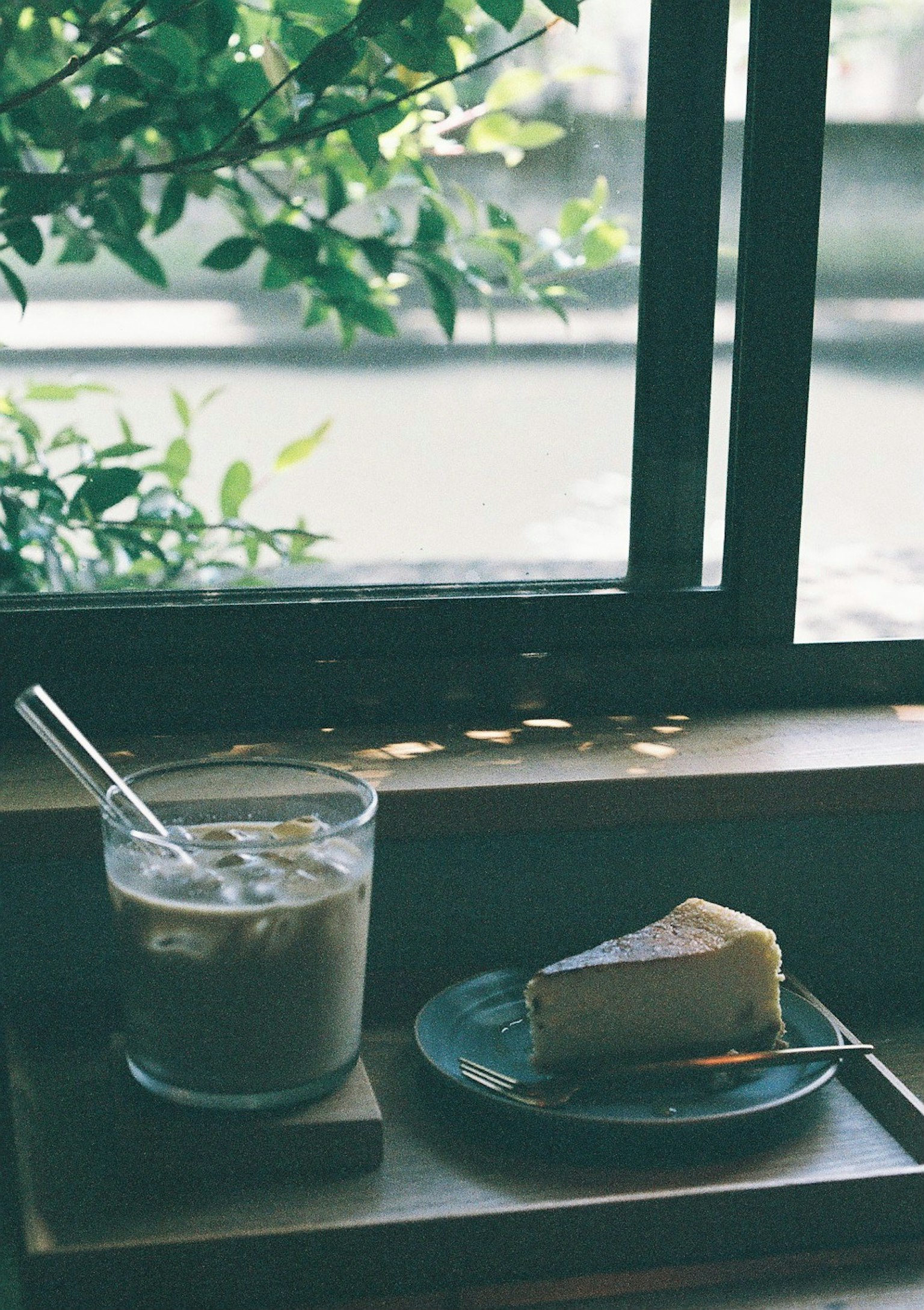 Caffè freddo e cheesecake su un piatto vicino alla finestra