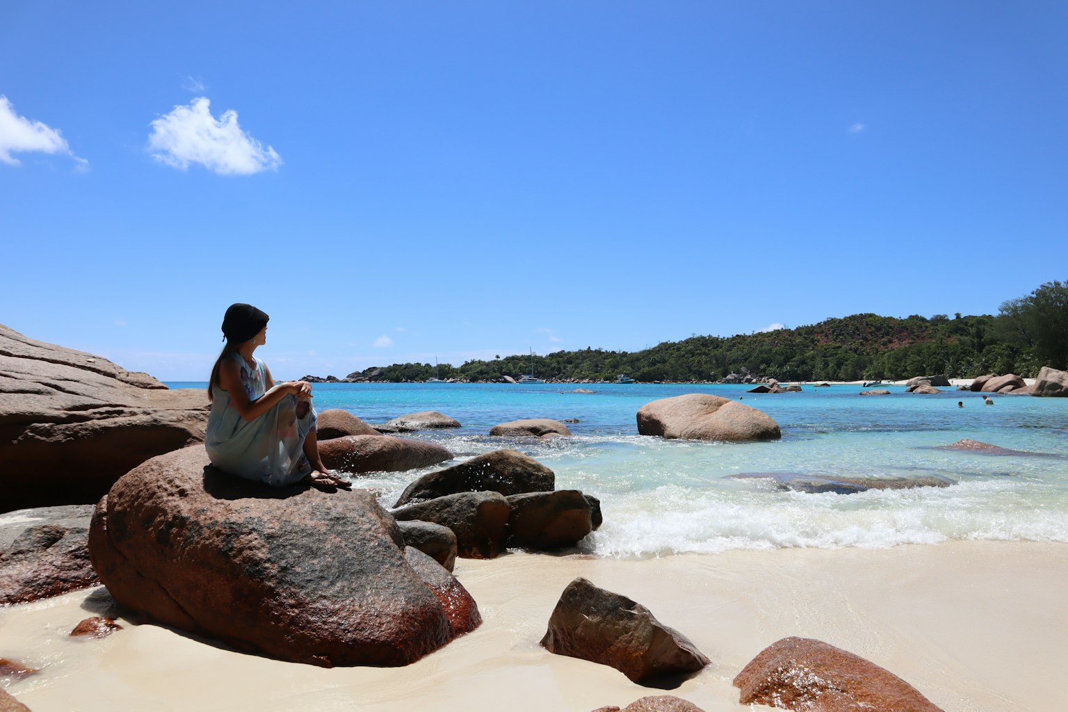 Une femme assise sur un rocher près de la mer bleue et de la plage de sable blanc