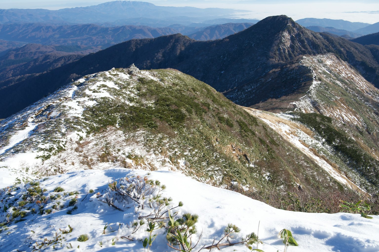 Snow-covered mountain landscape featuring lush green slopes and distant peaks
