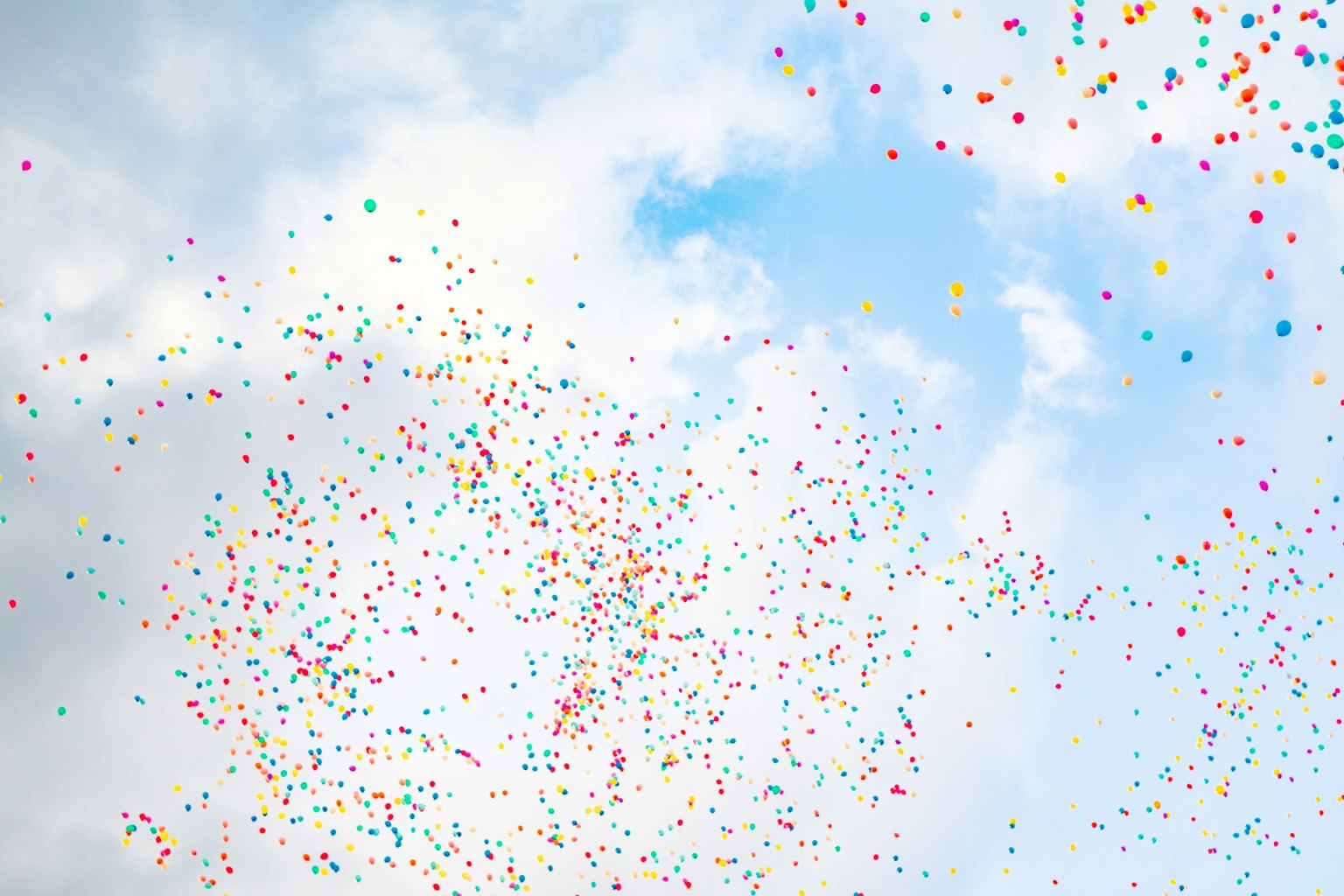 Balon berwarna-warni mengapung di langit biru dengan awan berbulu