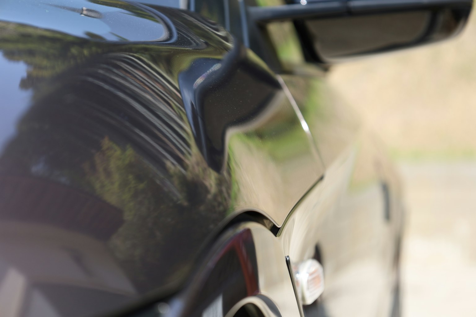 검은색 자동차의 측면 근접 사진으로 광택 있는 표면과 주변 반사가 보인다