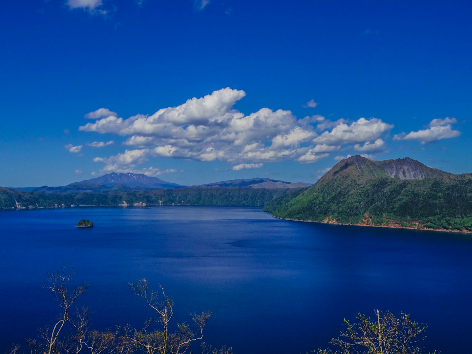 Pemandangan danau biru dikelilingi gunung dengan awan putih di langit
