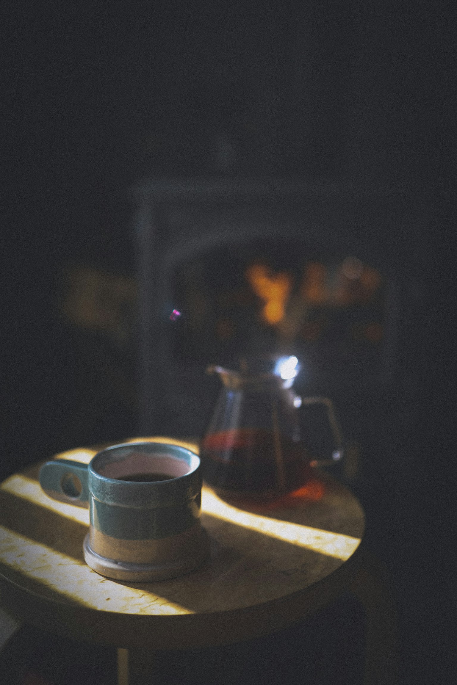 A coffee cup and teapot on a wooden table with warm lighting