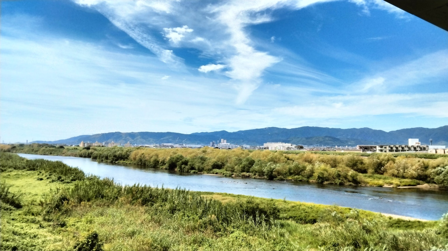 Vista escénica de un río con vegetación exuberante y montañas distantes bajo un cielo azul