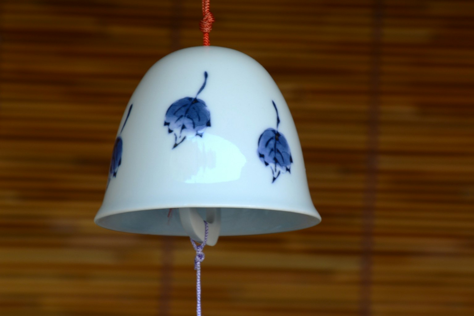 White ceramic bell with blue floral patterns hanging against a wooden background