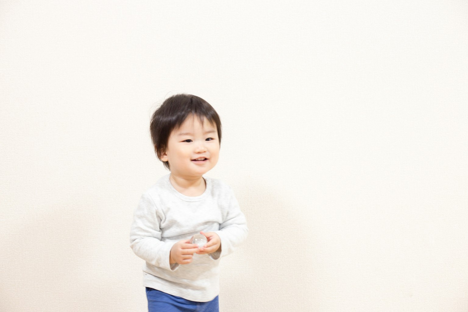 เด็กเล็กยิ้มขณะยืนอยู่หน้าพื้นหลังที่เรียบง่าย