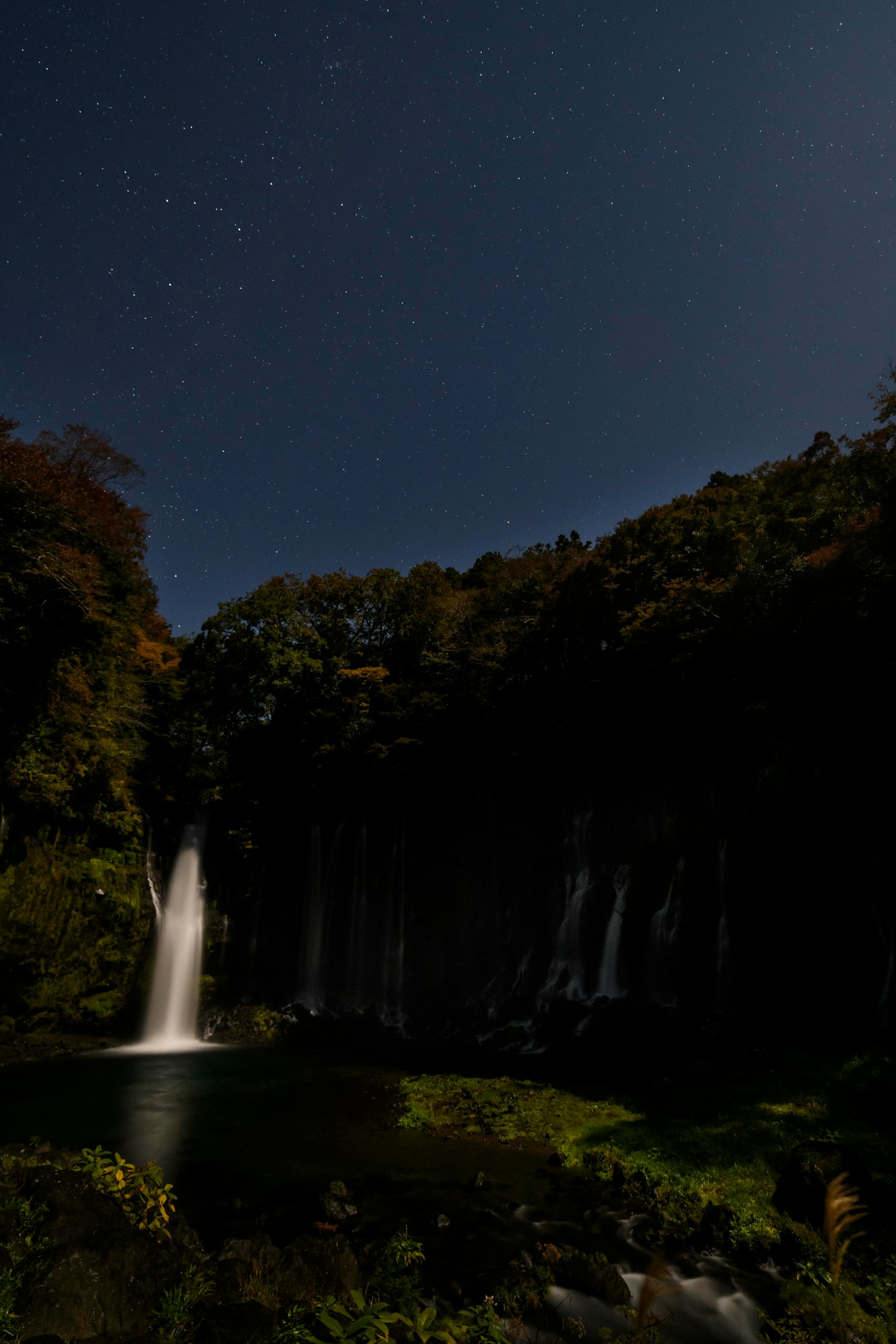 Una cascada iluminada por la luz de la luna en un cielo nocturno estrellado