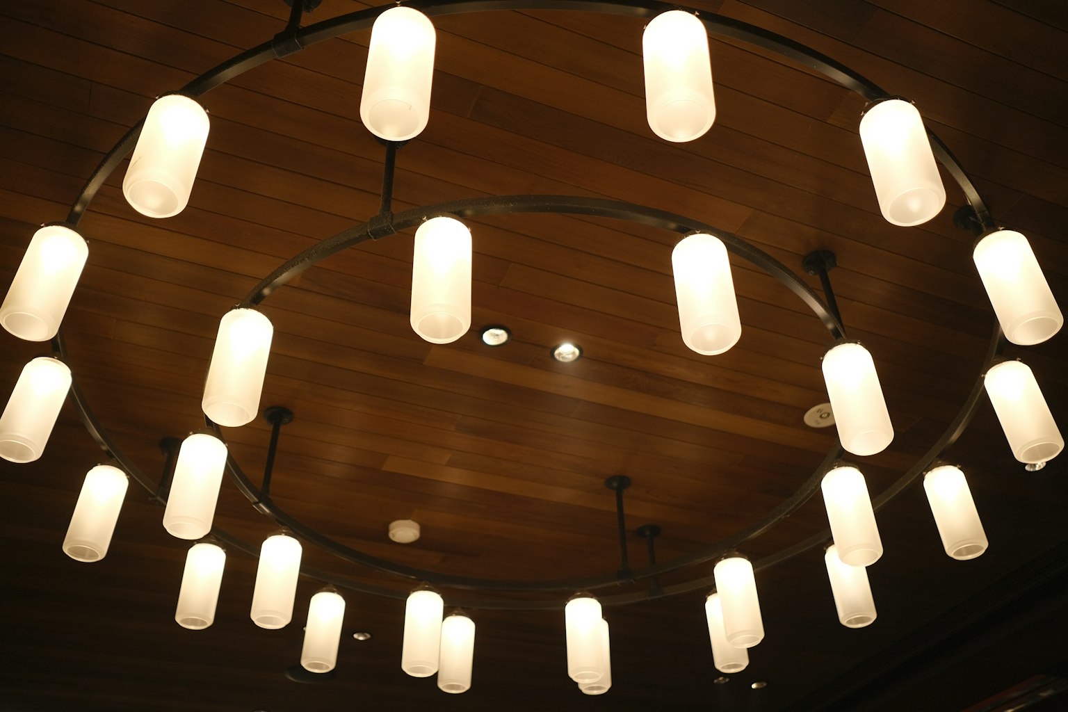 Circular ceiling light fixture with white shades hanging from wooden ceiling