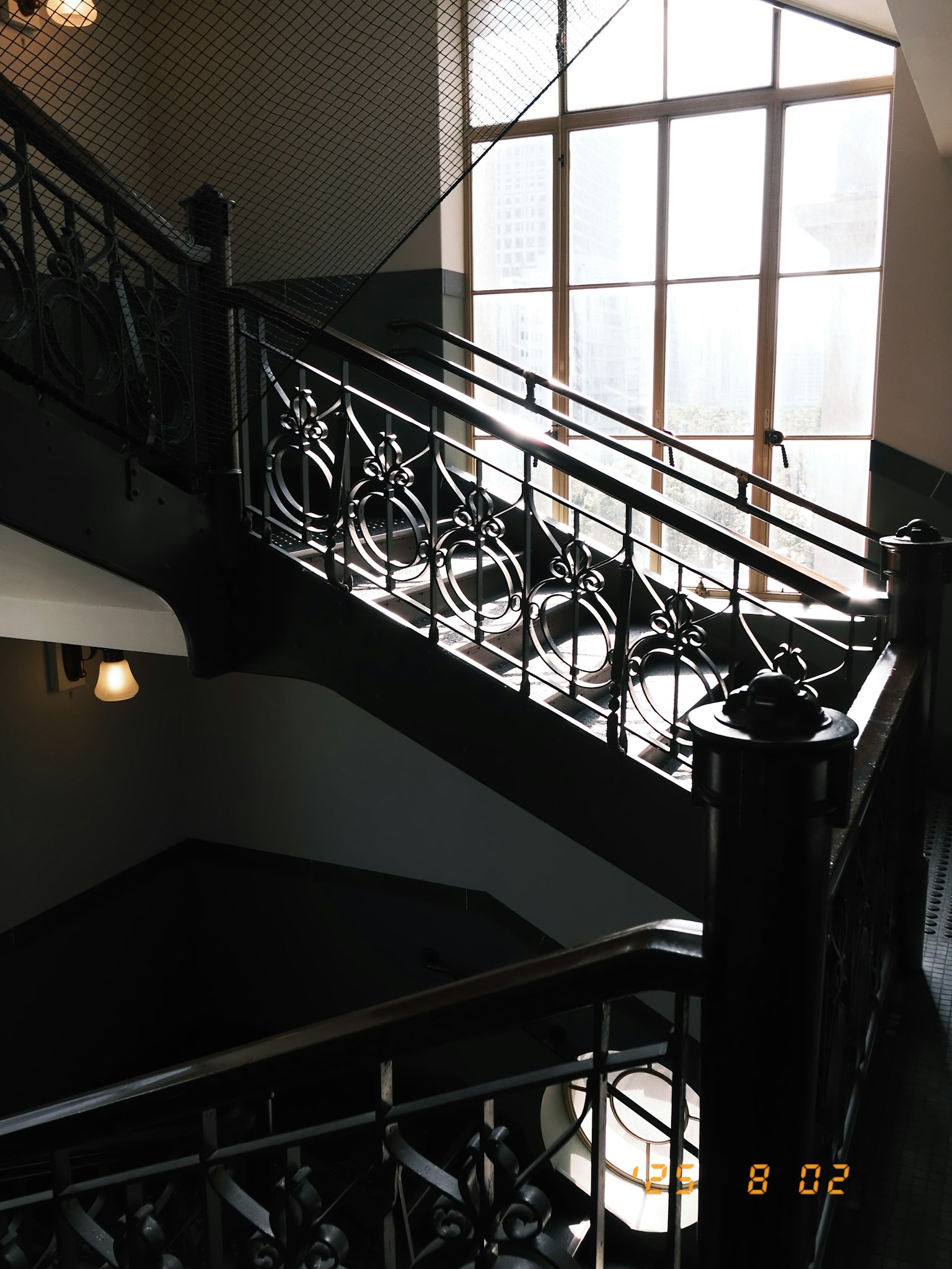 Vista interior de una escalera con barandilla ornamentada y gran ventana