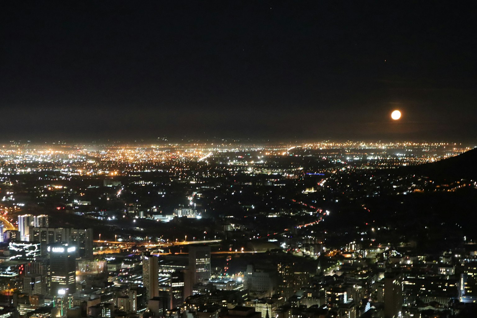 Vista nocturna de un paisaje urbano con montañas y una luna creciente