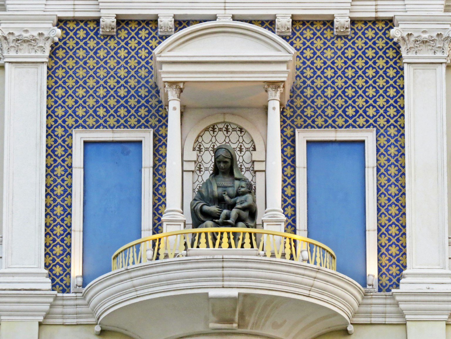 Estatua de María con el niño en un balcón rodeado de azulejos decorativos