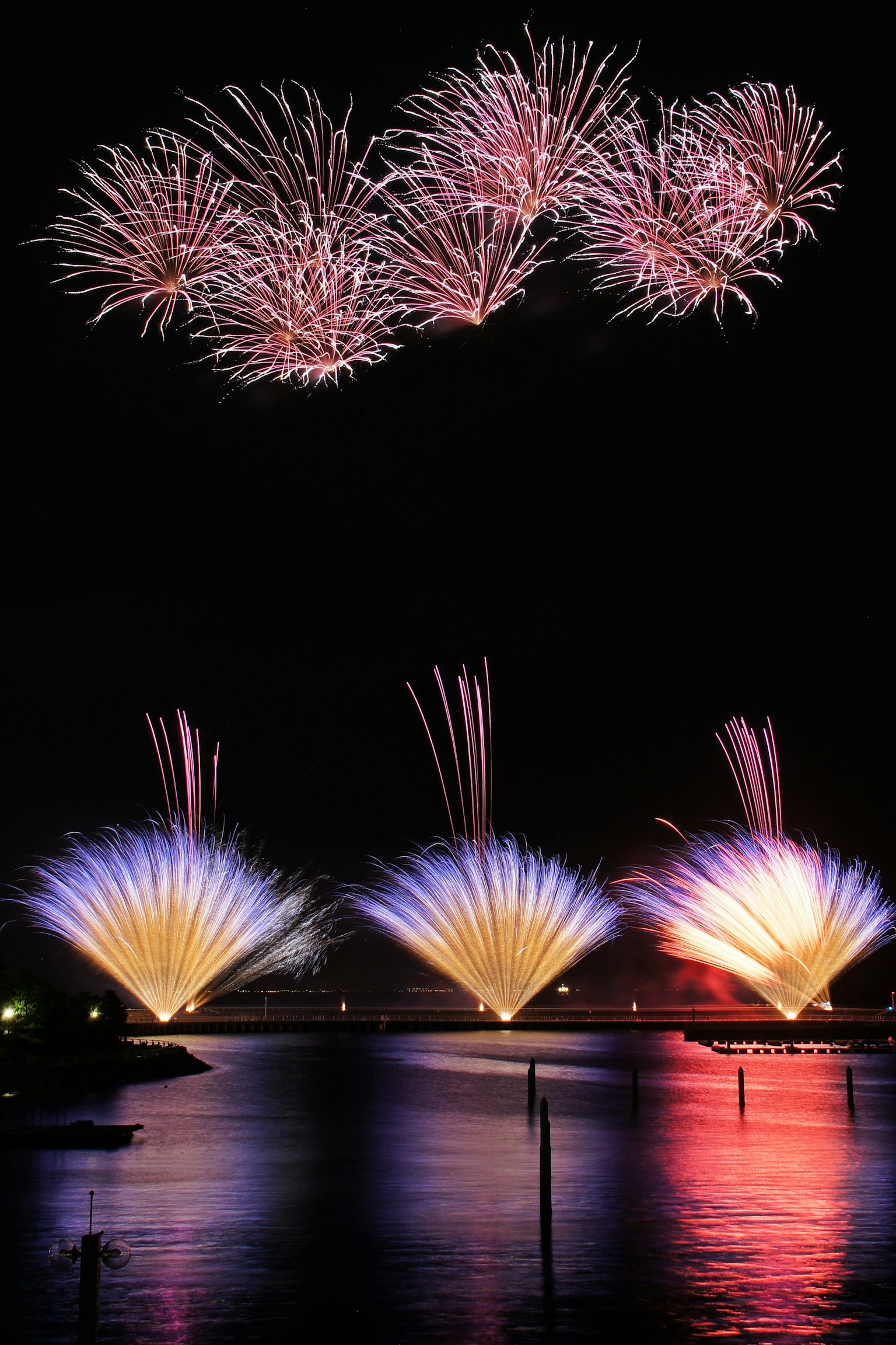 Fuochi d'artificio che illuminano il cielo notturno con riflessi colorati sull'acqua