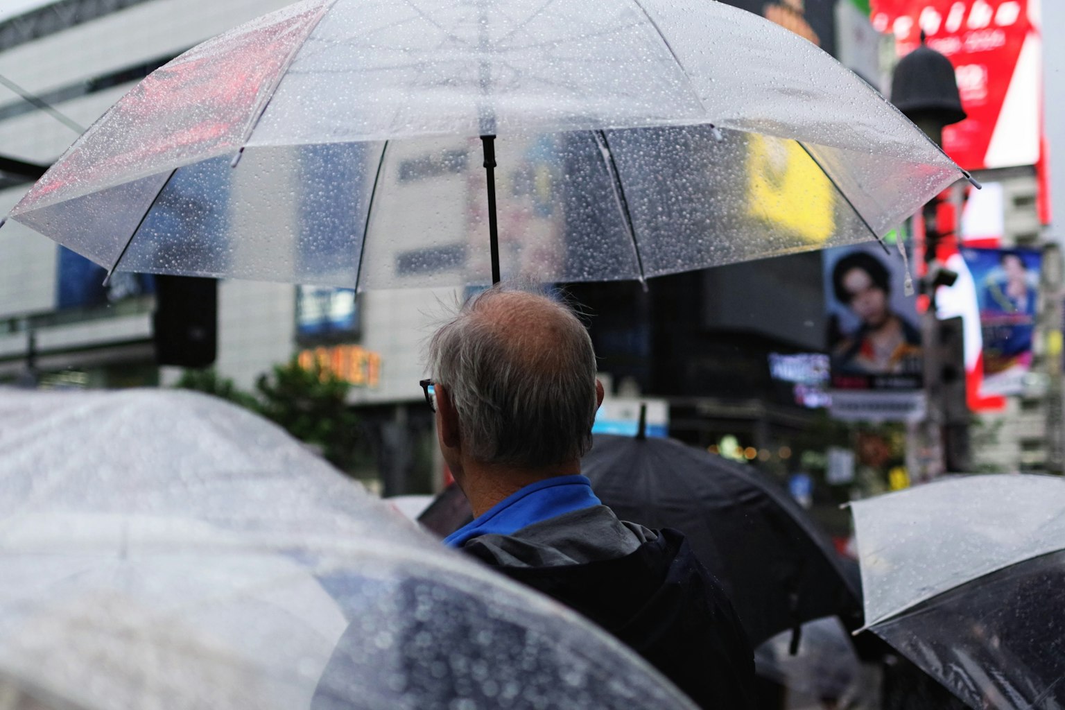 一名男子在雨中撐著傘，周圍有其他傘