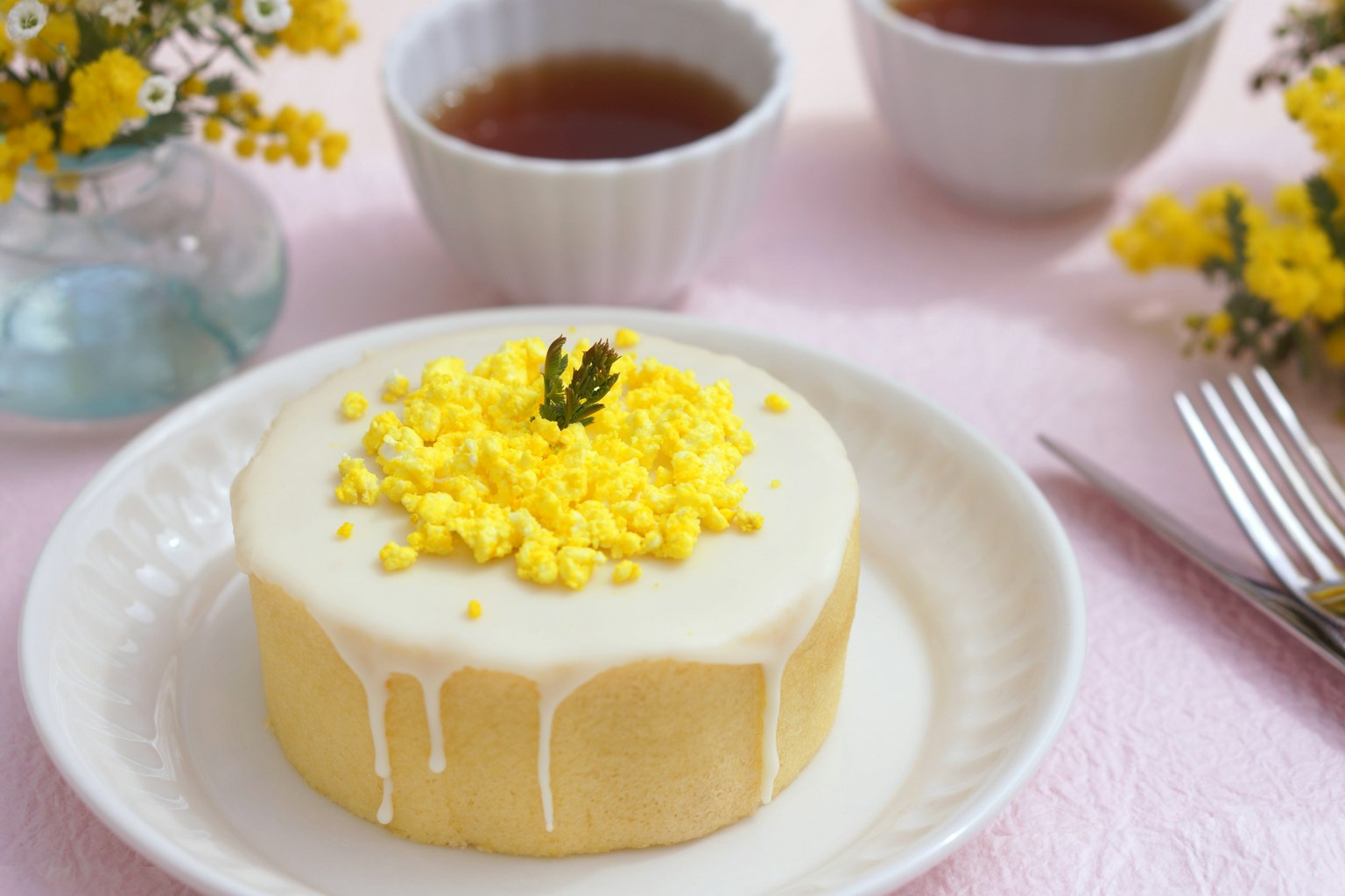 Ein Kuchen mit gelber Dekoration und Teetassen auf einem pastellfarbenen Tisch