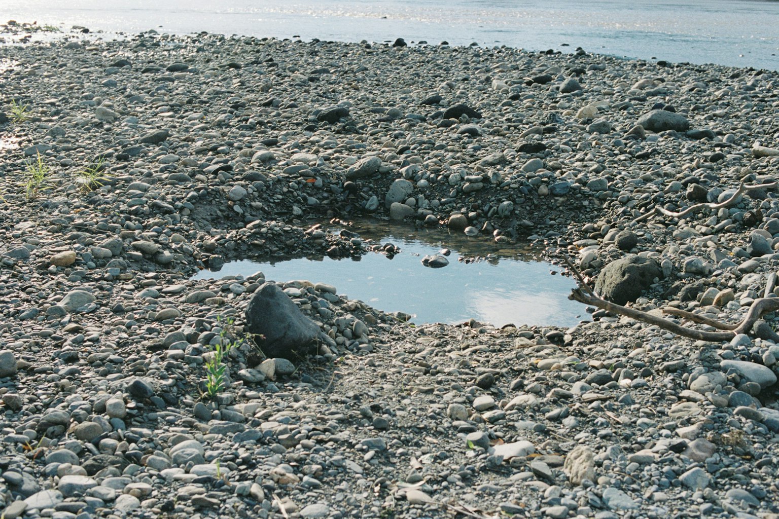 Kleine Pfütze umgeben von Steinen an einem kieseligen Strand