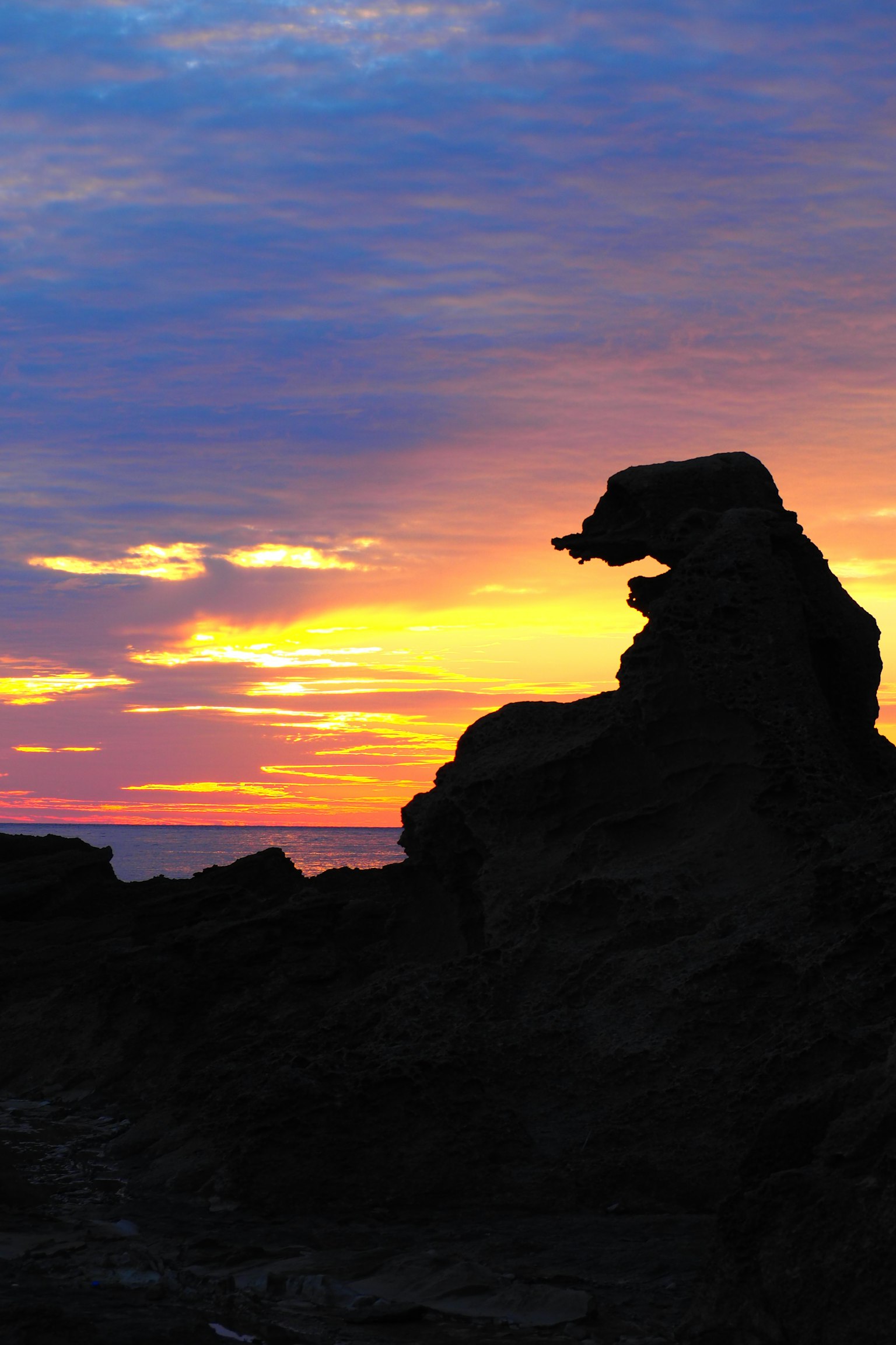 Silhouette einer Felsformation vor einem bunten Sonnenuntergang