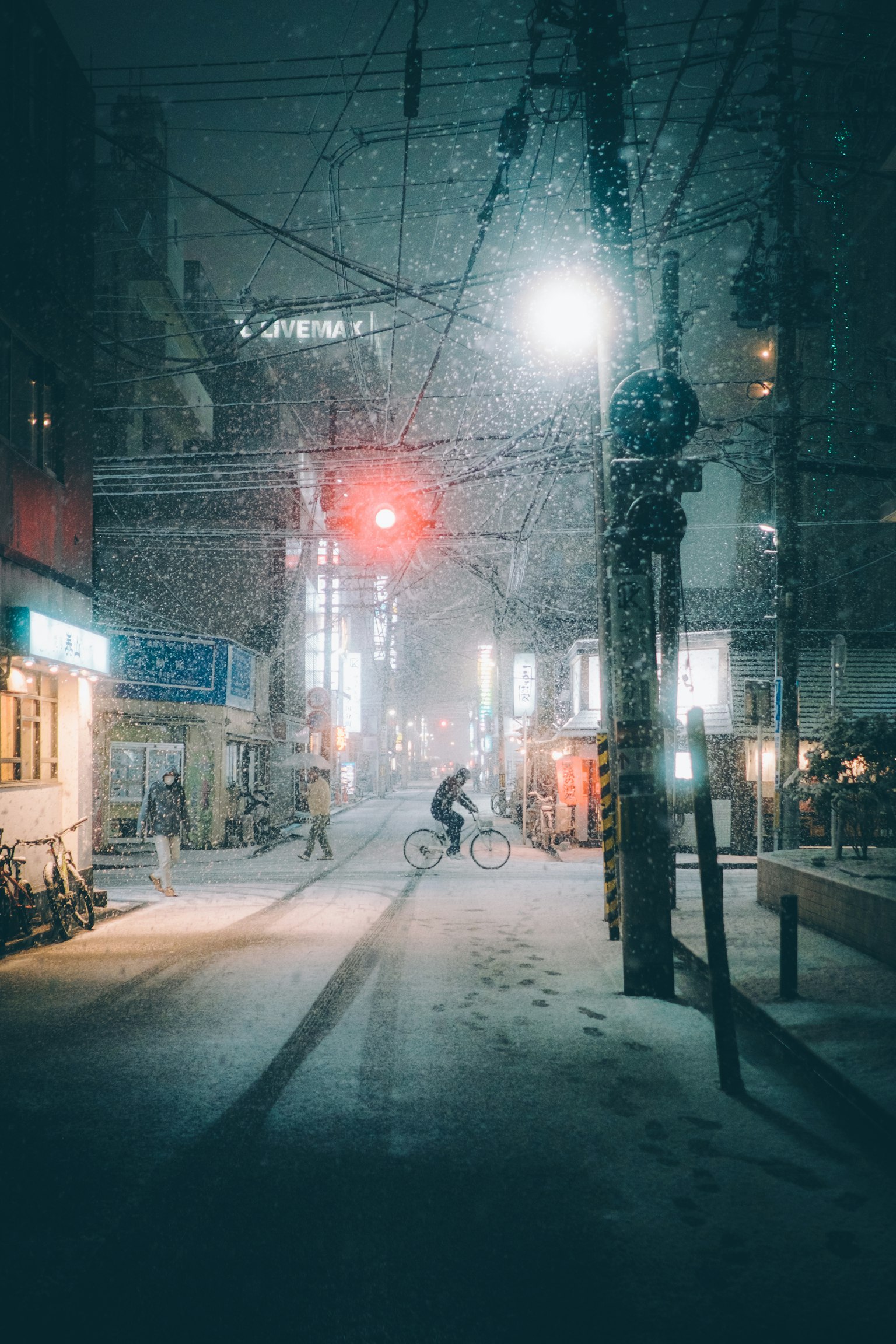一個人在雪夜的街道上騎自行車，紅色交通信號燈