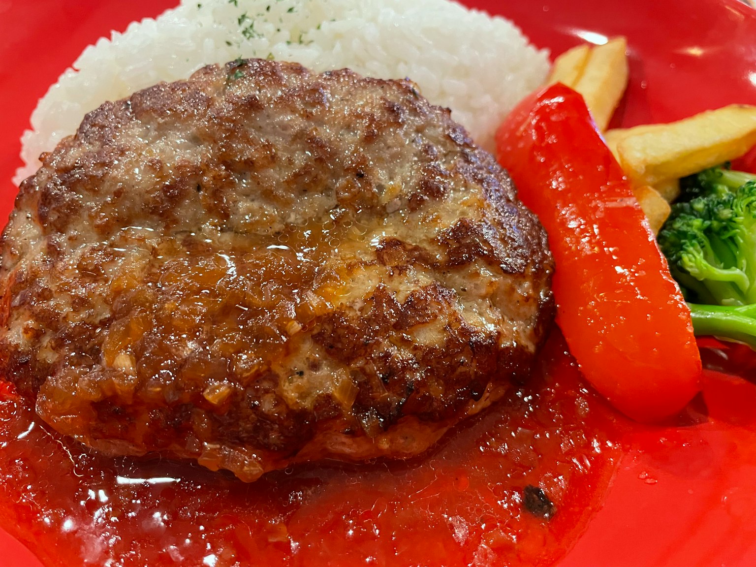 Un hamburger servito su un piatto rosso con riso broccoli e peperone rosso
