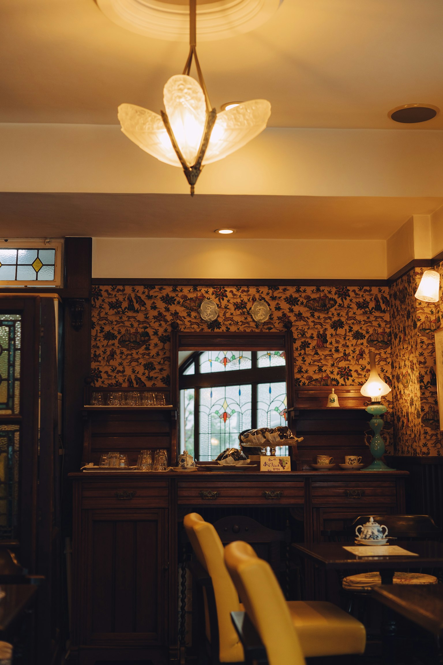 Interior de un café retro con lámpara en forma de flor, muebles de madera, papel tapiz estampado, luz natural de la ventana