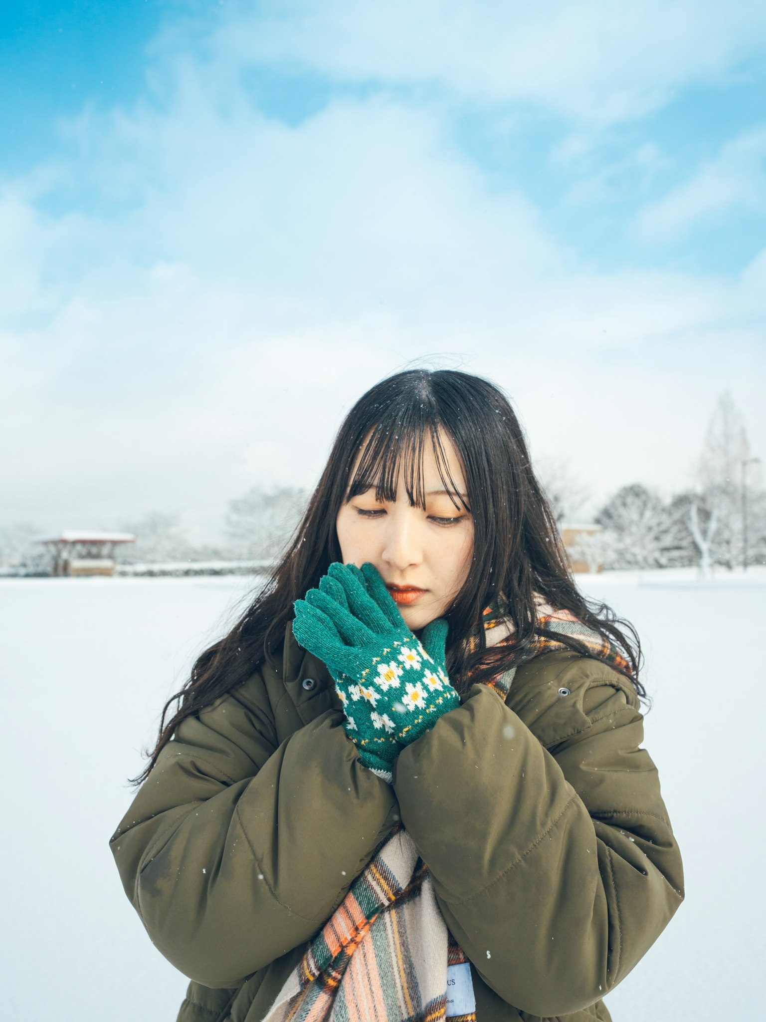 Woman warming her hands in the snow wearing green gloves winter landscape