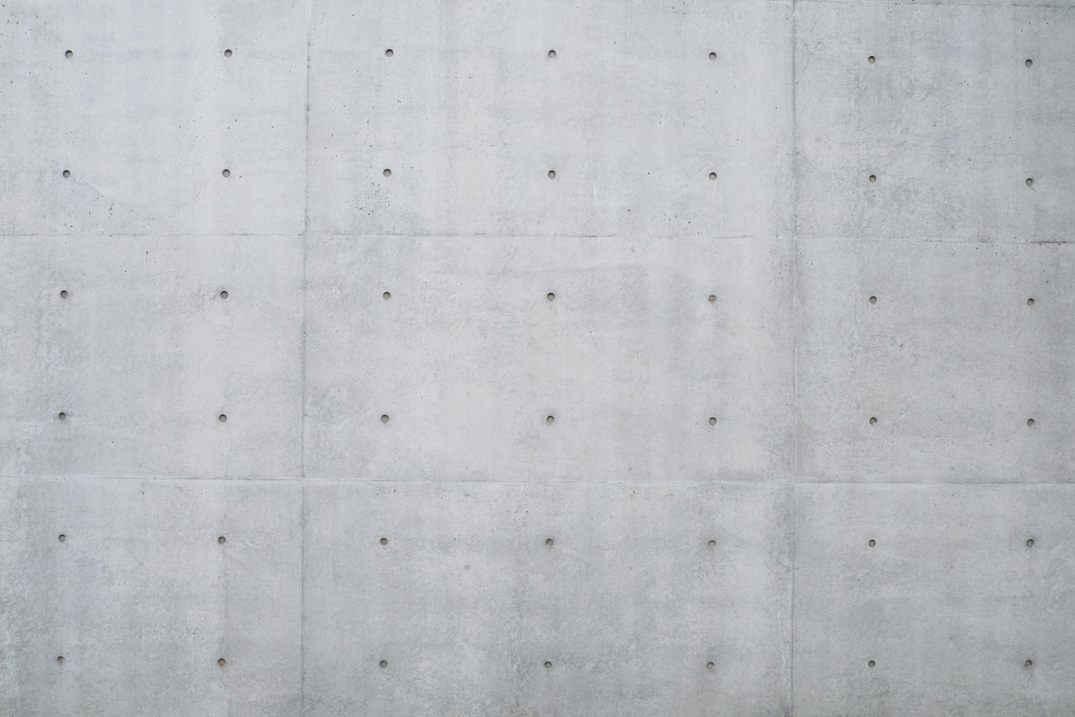 Graue Betonwand mit gleichmäßig verteilten kleinen Metallschrauben