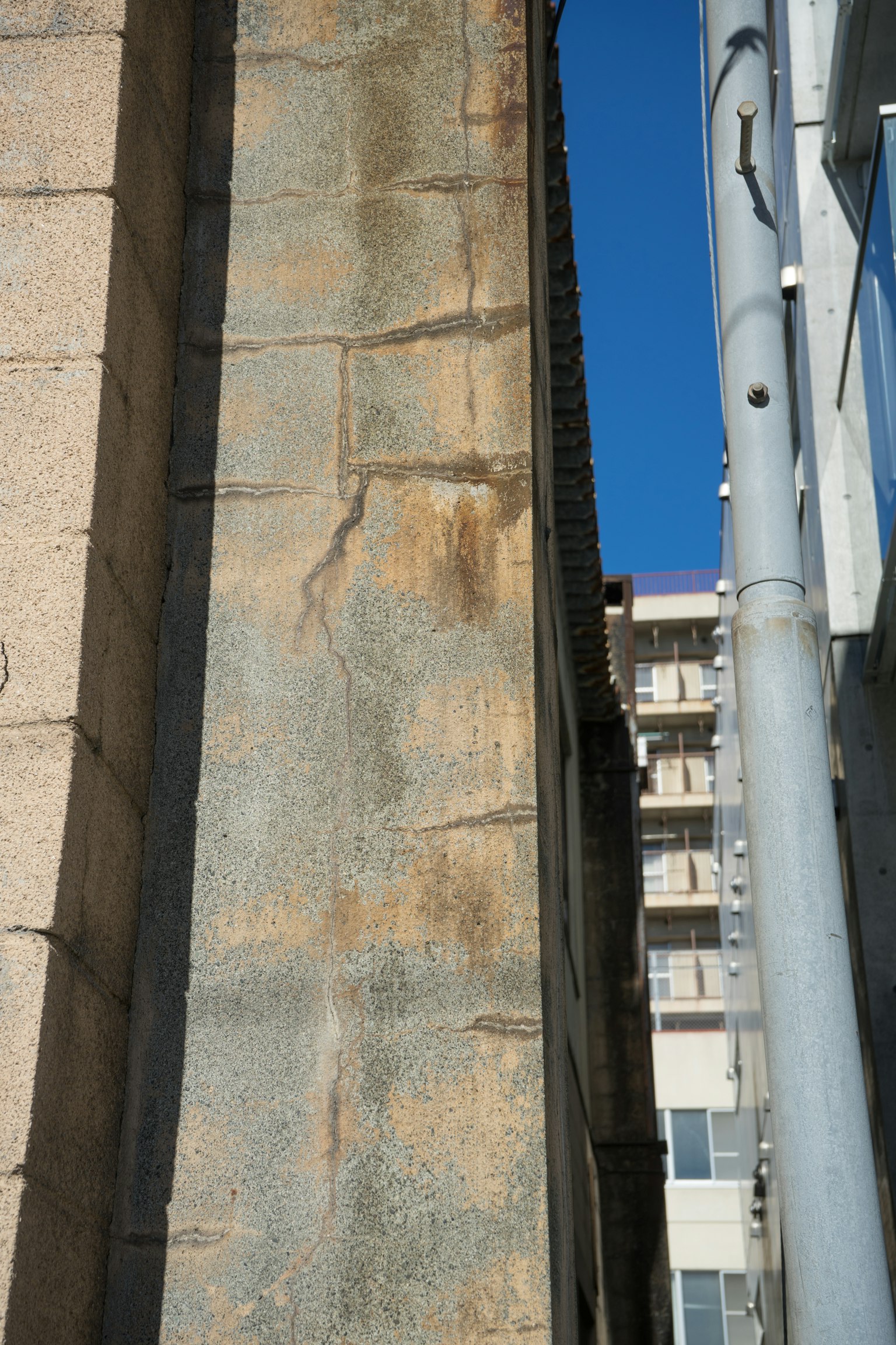Primer plano de una pared de edificio bajo un cielo azul que destaca el contraste entre piedra antigua y estructura moderna