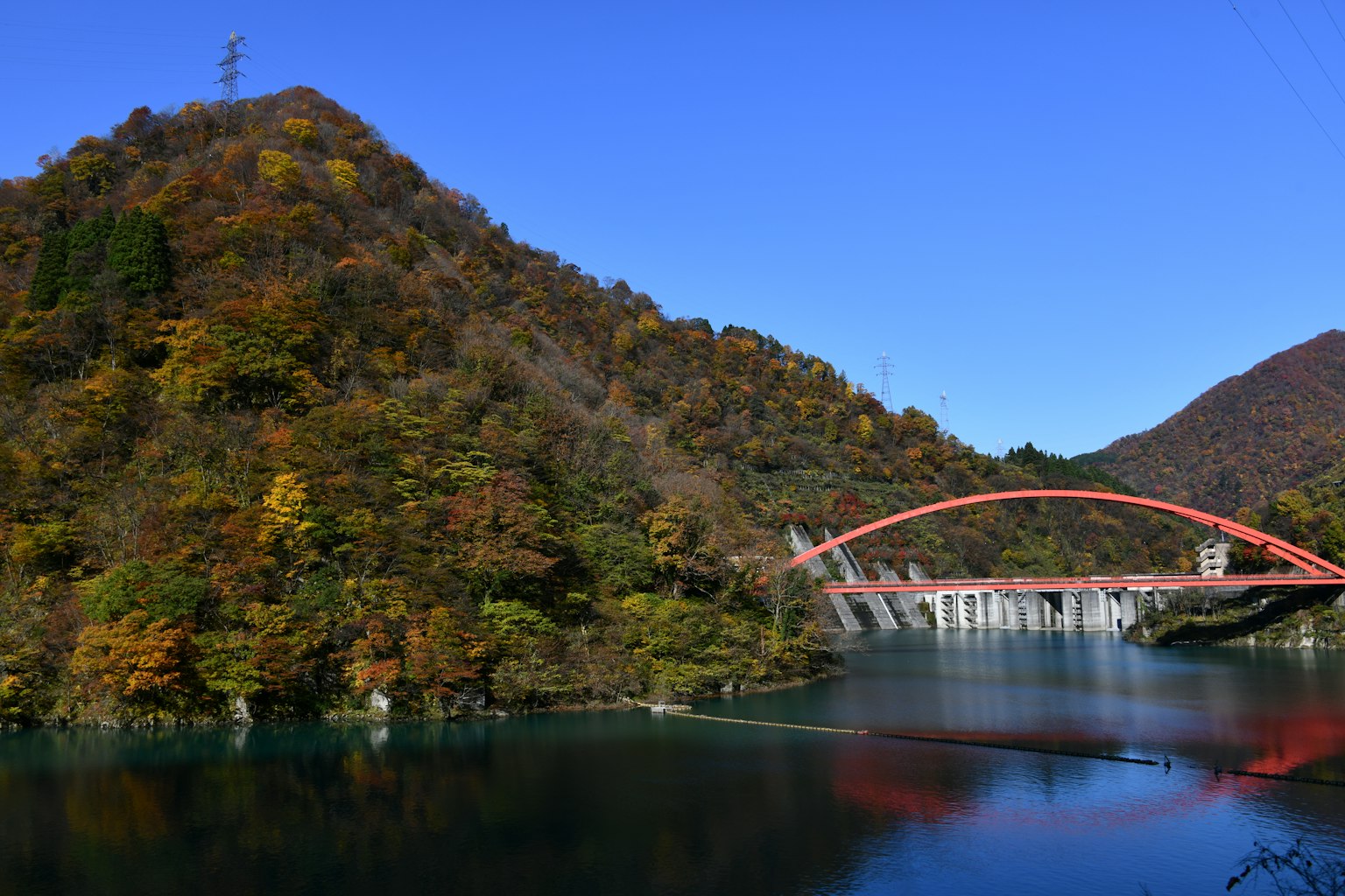 Scenic view of a mountain with autumn colors and a striking red arch bridge