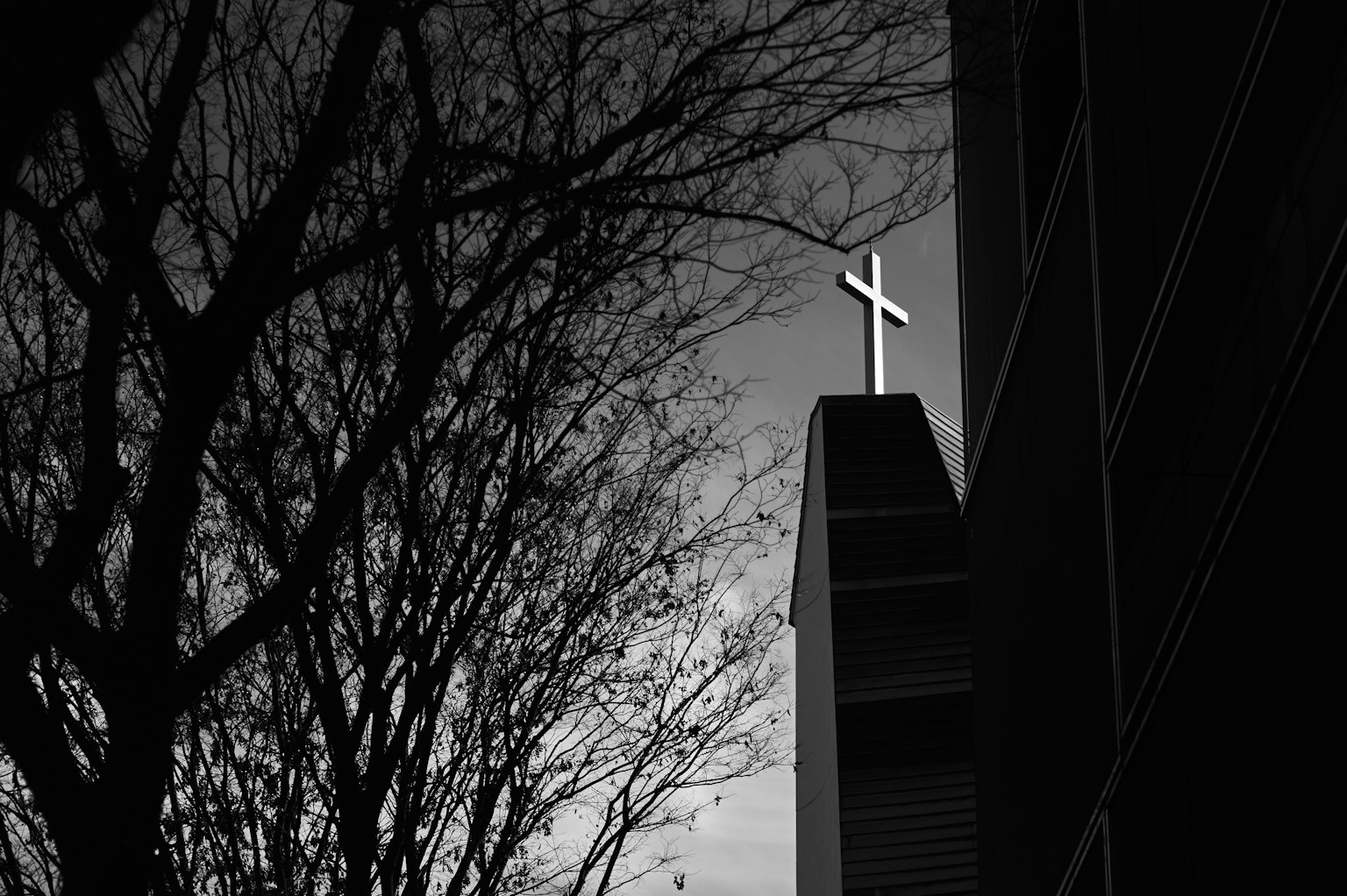 Siluet salib di atas gereja dengan pohon telanjang di latar depan