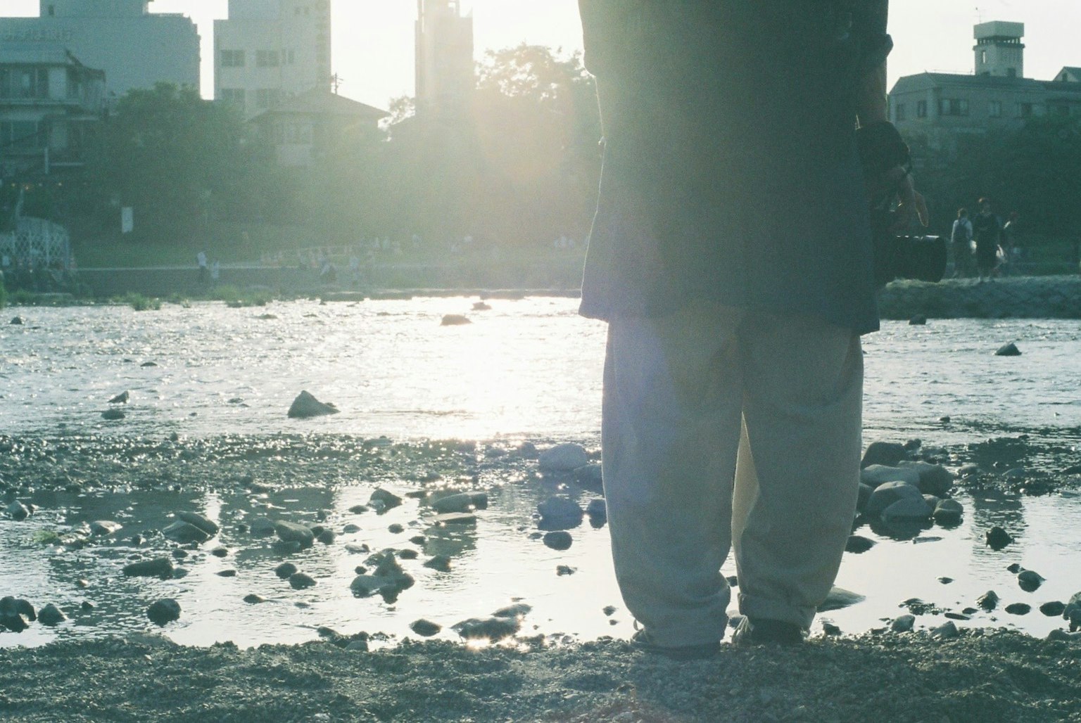 Photo of a person standing on the riverbank with their back to the camera